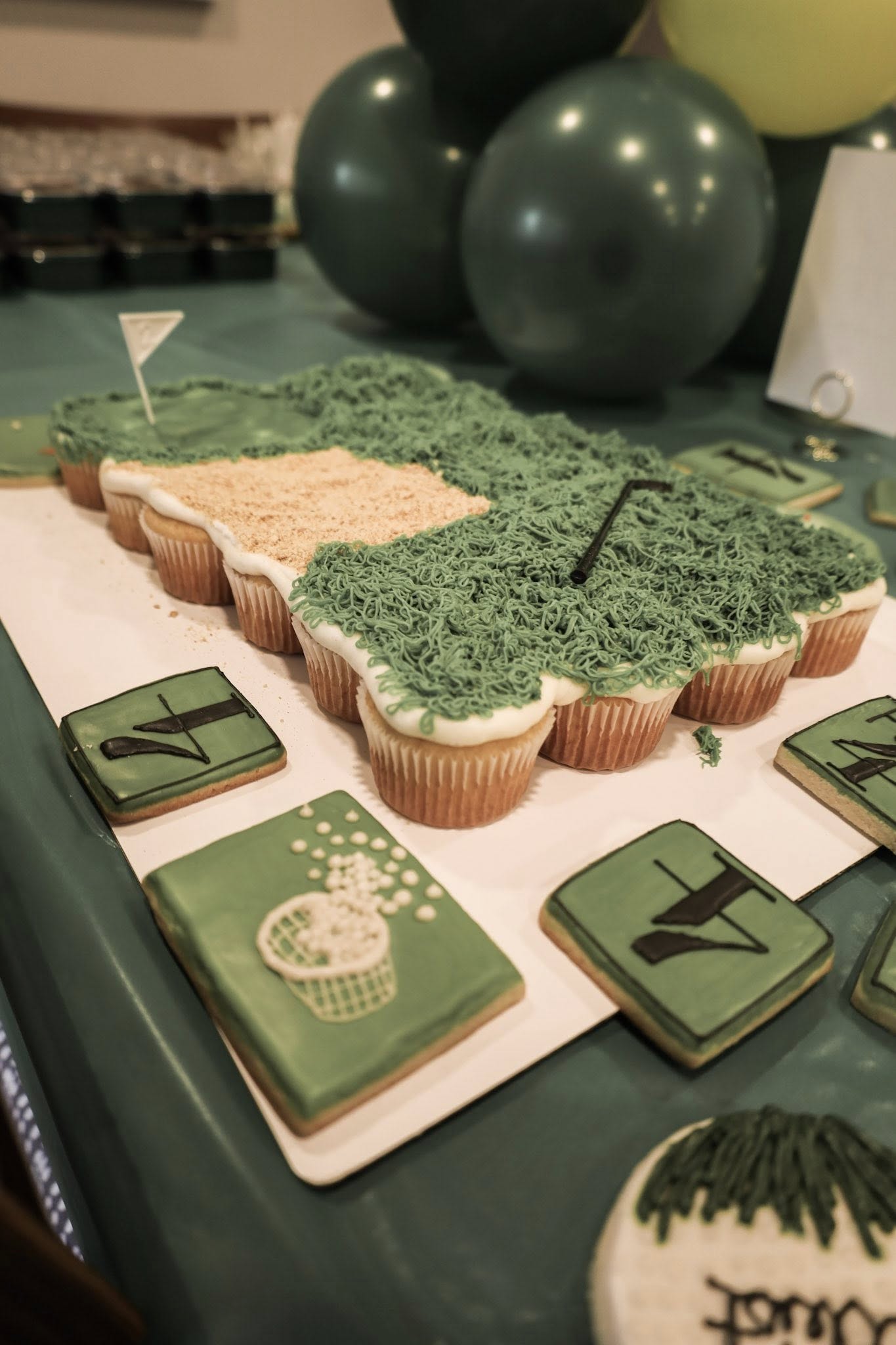 Golf-themed pull-apart cupcake cake shaped like a putting green with decorative golf-themed sugar cookies nearby.