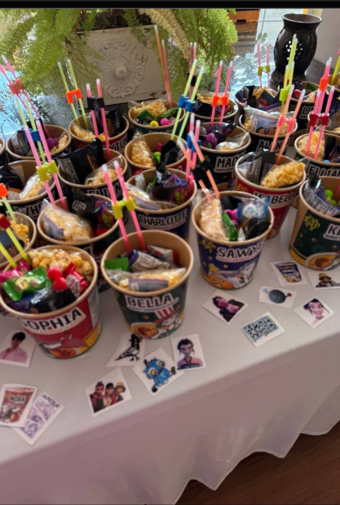Personalized snack buckets with names and glow sticks arranged on a table with party stickers.