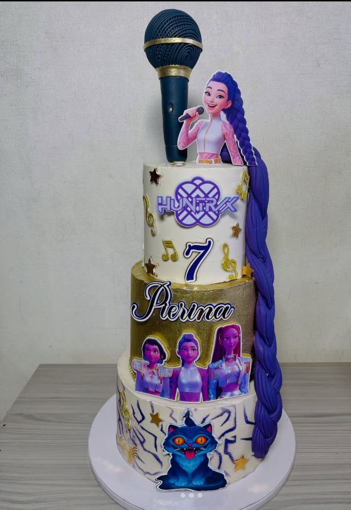 Three-tiered birthday cake themed with Huntrix characters, musical notes, and a large microphone cake topper.