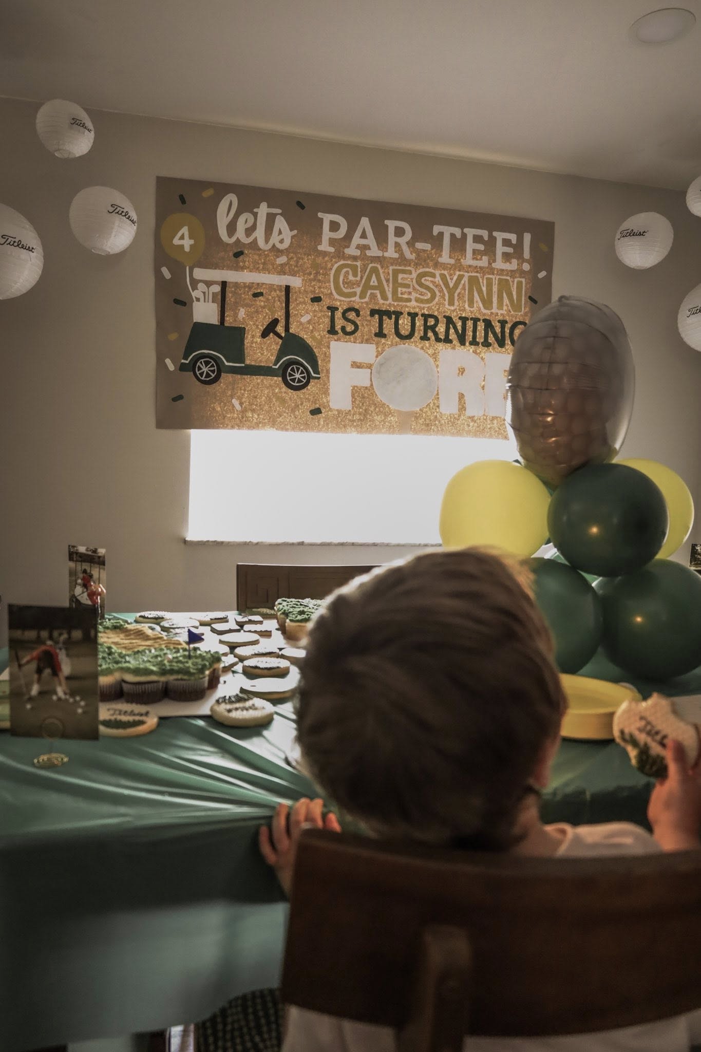 Child sitting at a golf-themed fourth birthday party with a banner reading Lets Par-Tee Caenynn is Turning Fore