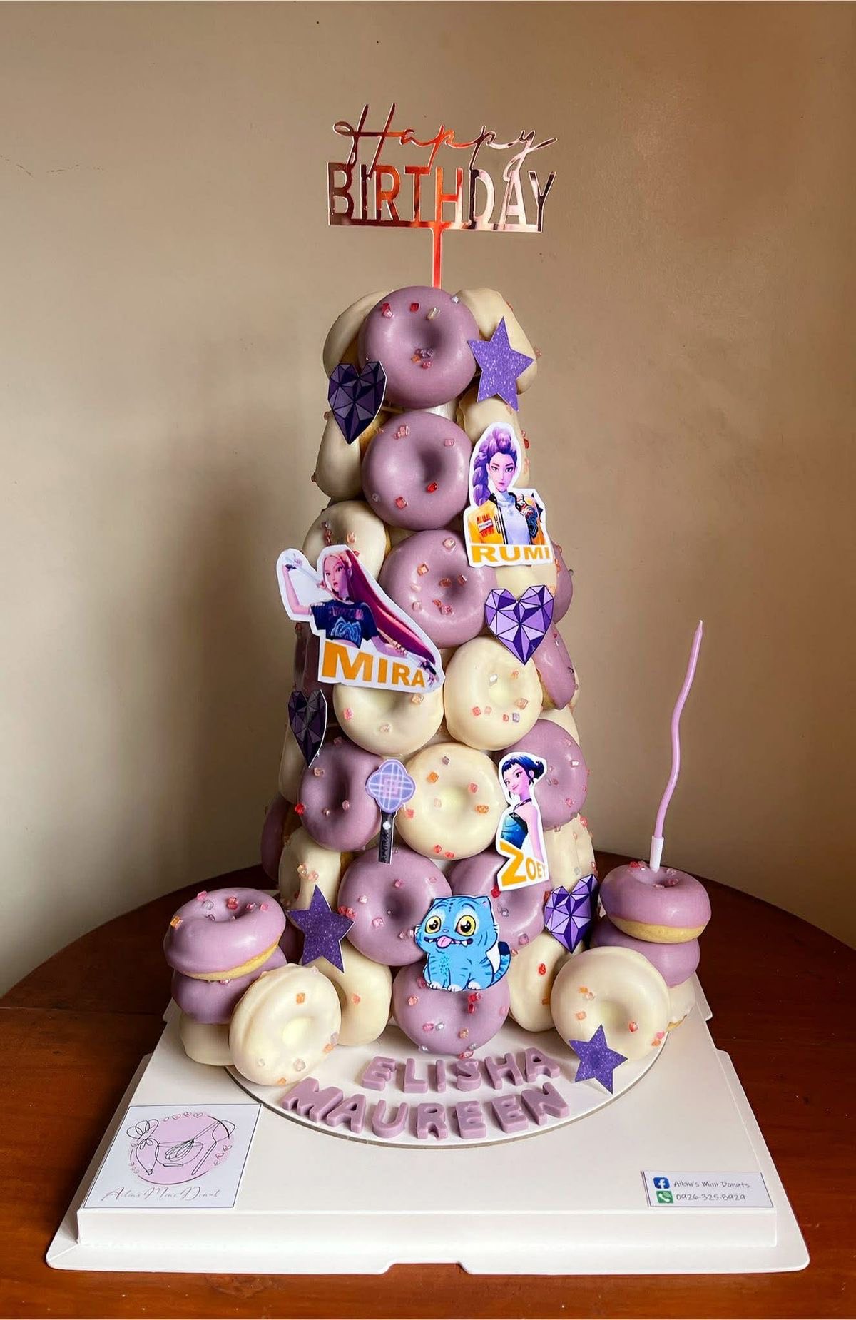 Mini donut tower cake decorated with purple and white icing, birthday toppers, and character cutouts.