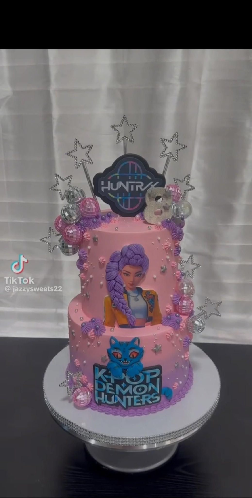Two-tier pink K-Pop Demon Hunters birthday cake decorated with disco balls and stars.