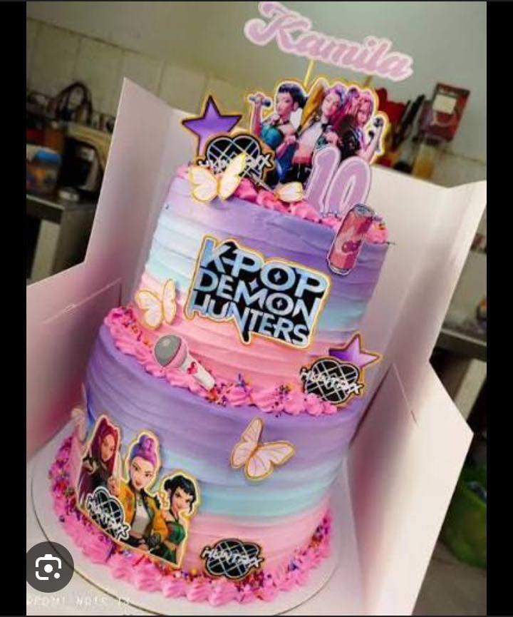 Two-tier K-Pop-themed birthday cake with purple and pink ombre icing, character toppers, and a name sign reading Kamila.