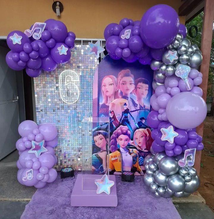 6th birthday party backdrop with purple balloons, silver sequin wall, and K-pop girl group character graphics.