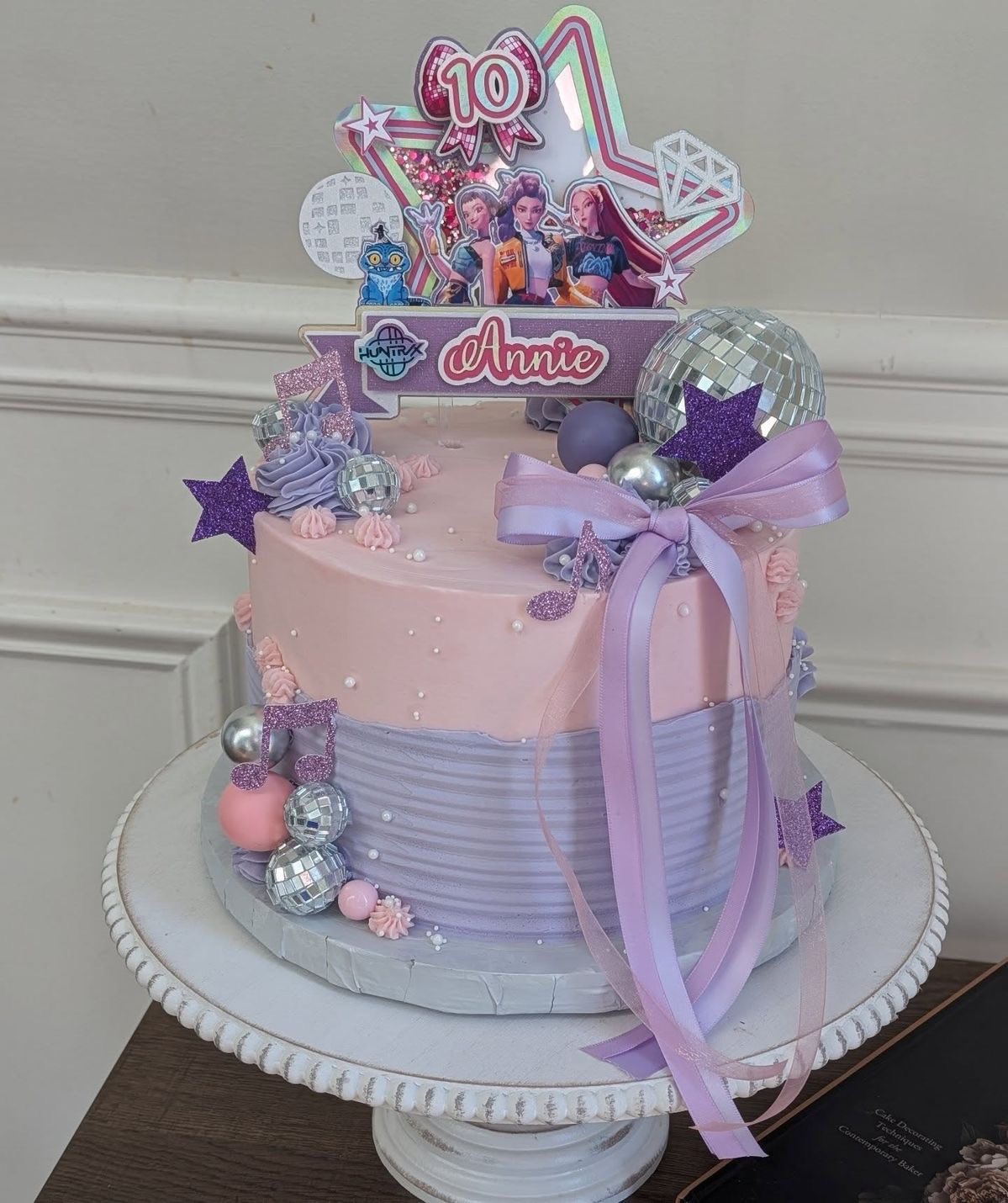 Two-tier pink and purple birthday cake decorated with disco balls, musical notes, and an Annie 10th birthday topper.