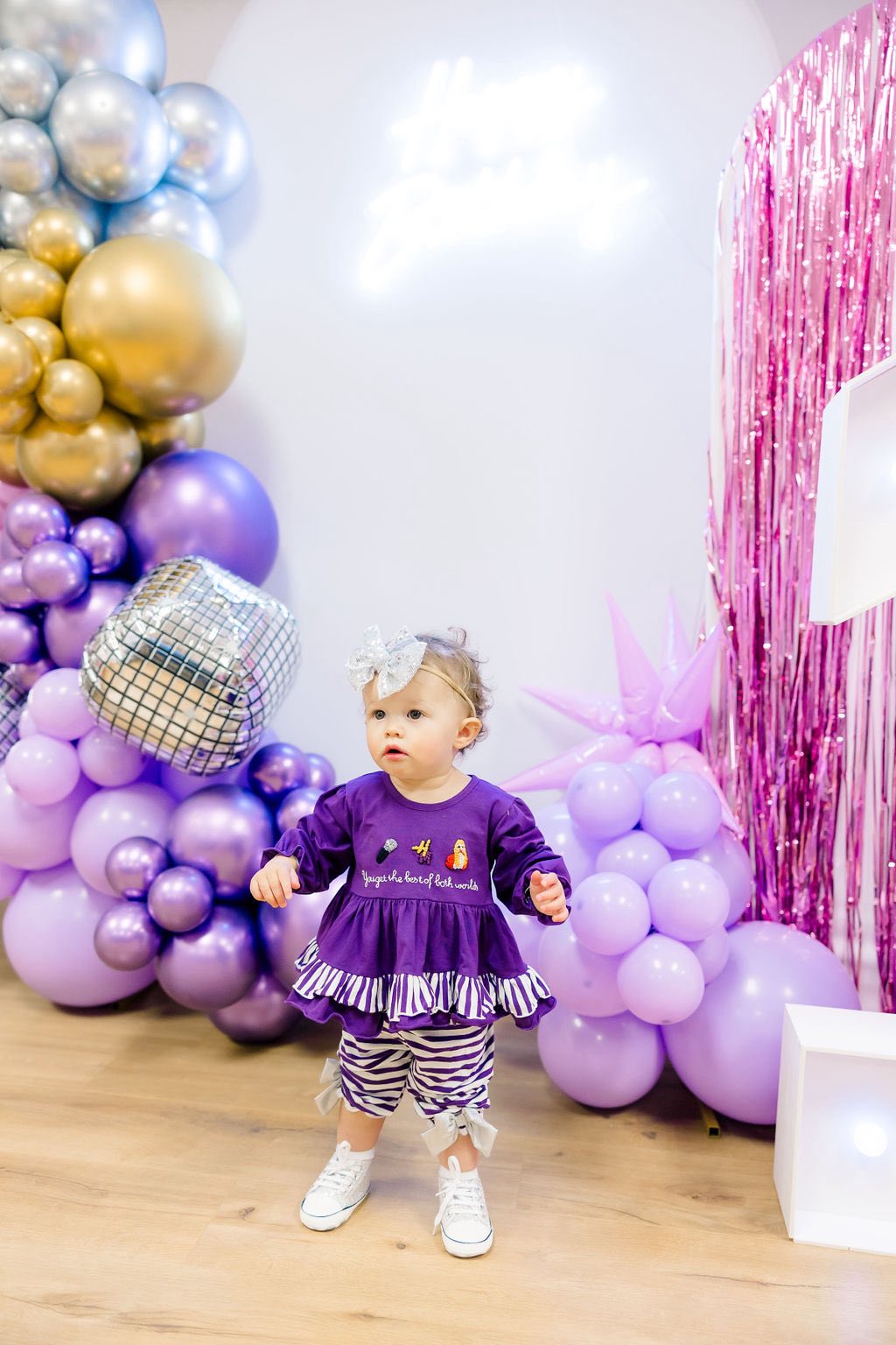 Toddler wearing a long-sleeve purple ruffled shirt with zebra print pants and a silver bow headband at a birthday party