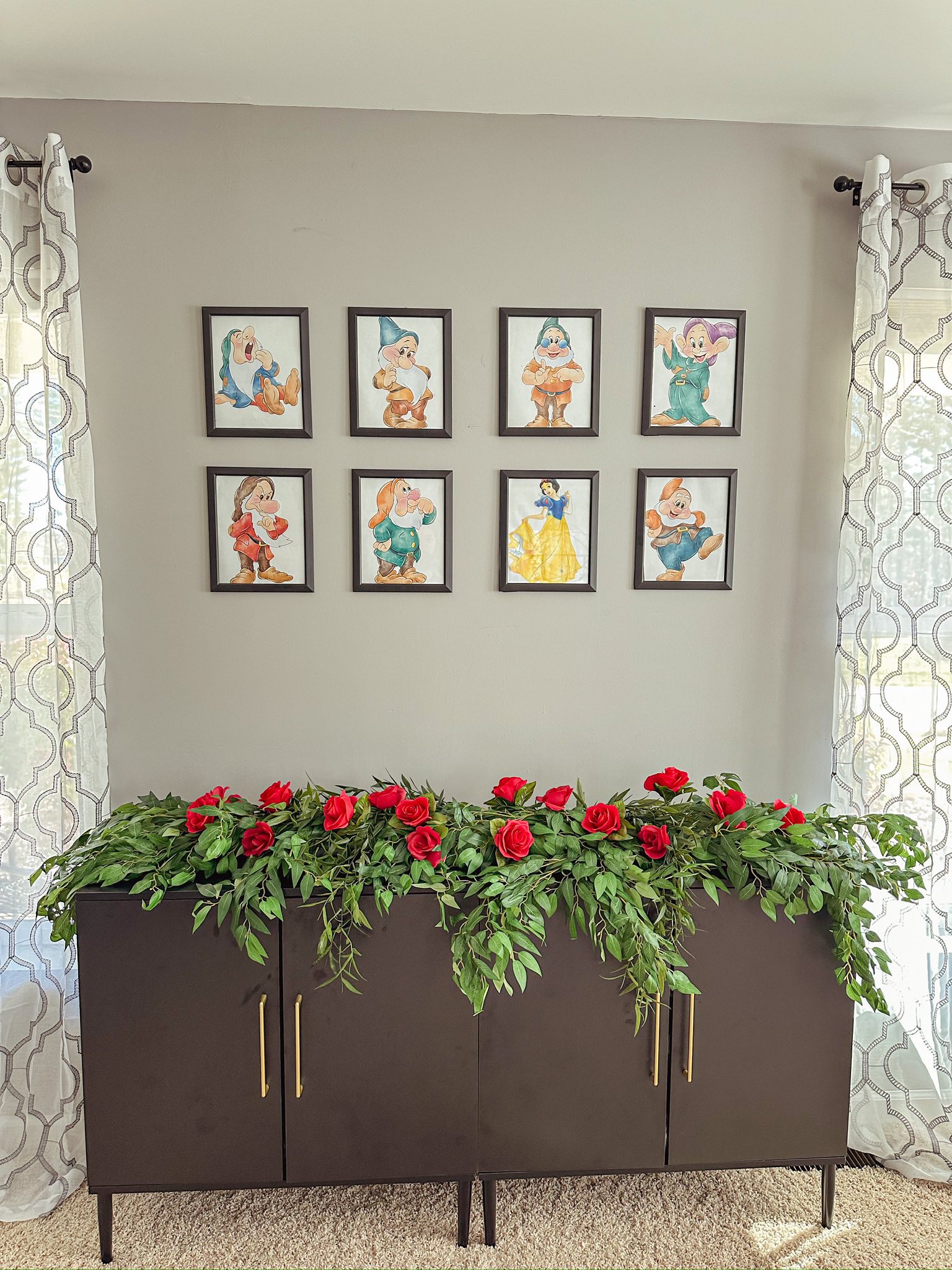 Gallery wall featuring framed prints of Snow White and the Seven Dwarfs above a sideboard decorated with red roses.