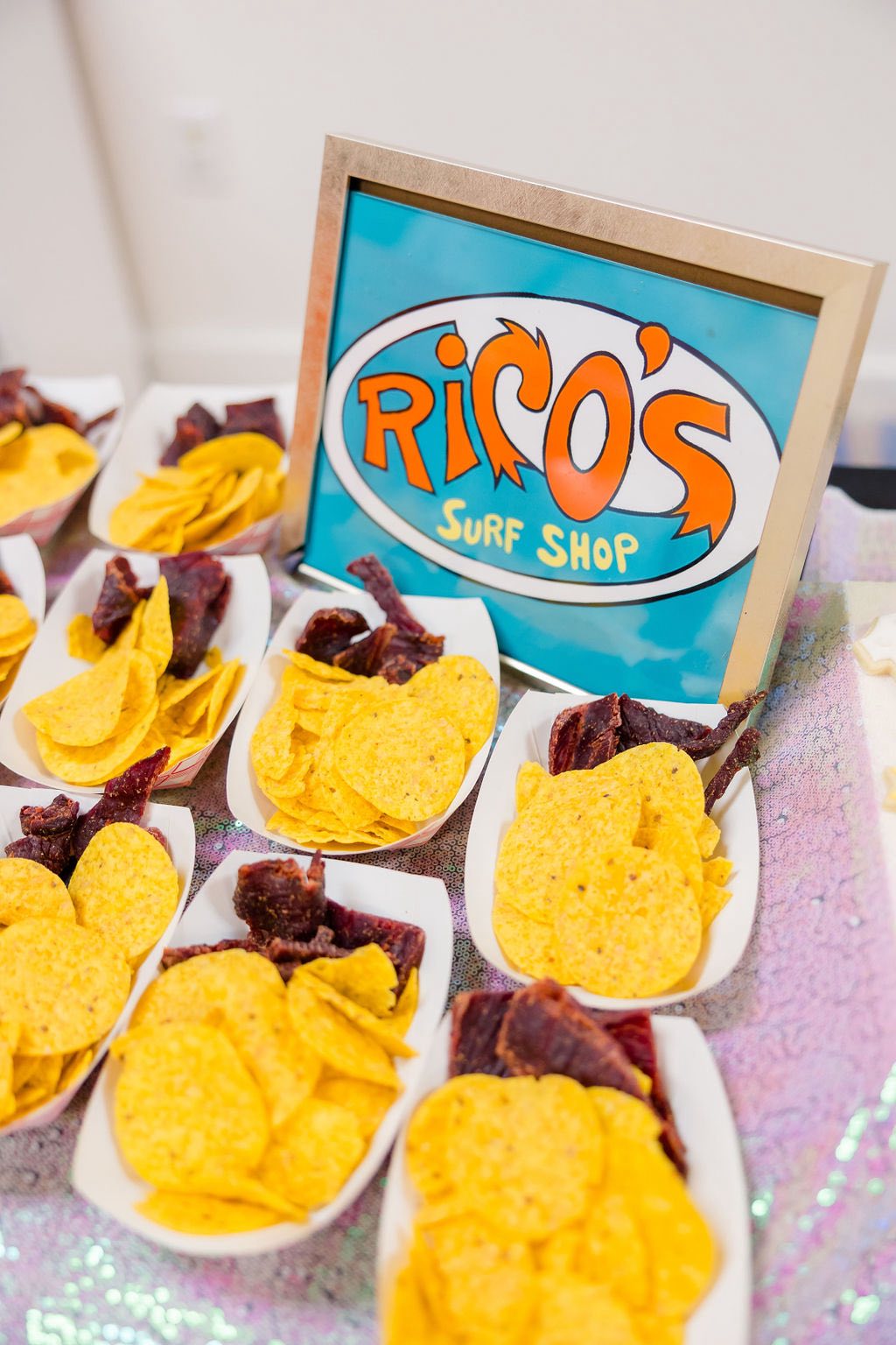 Rico's Surf Shop sign displayed next to individual snack trays filled with tortilla chips and beef jerky.