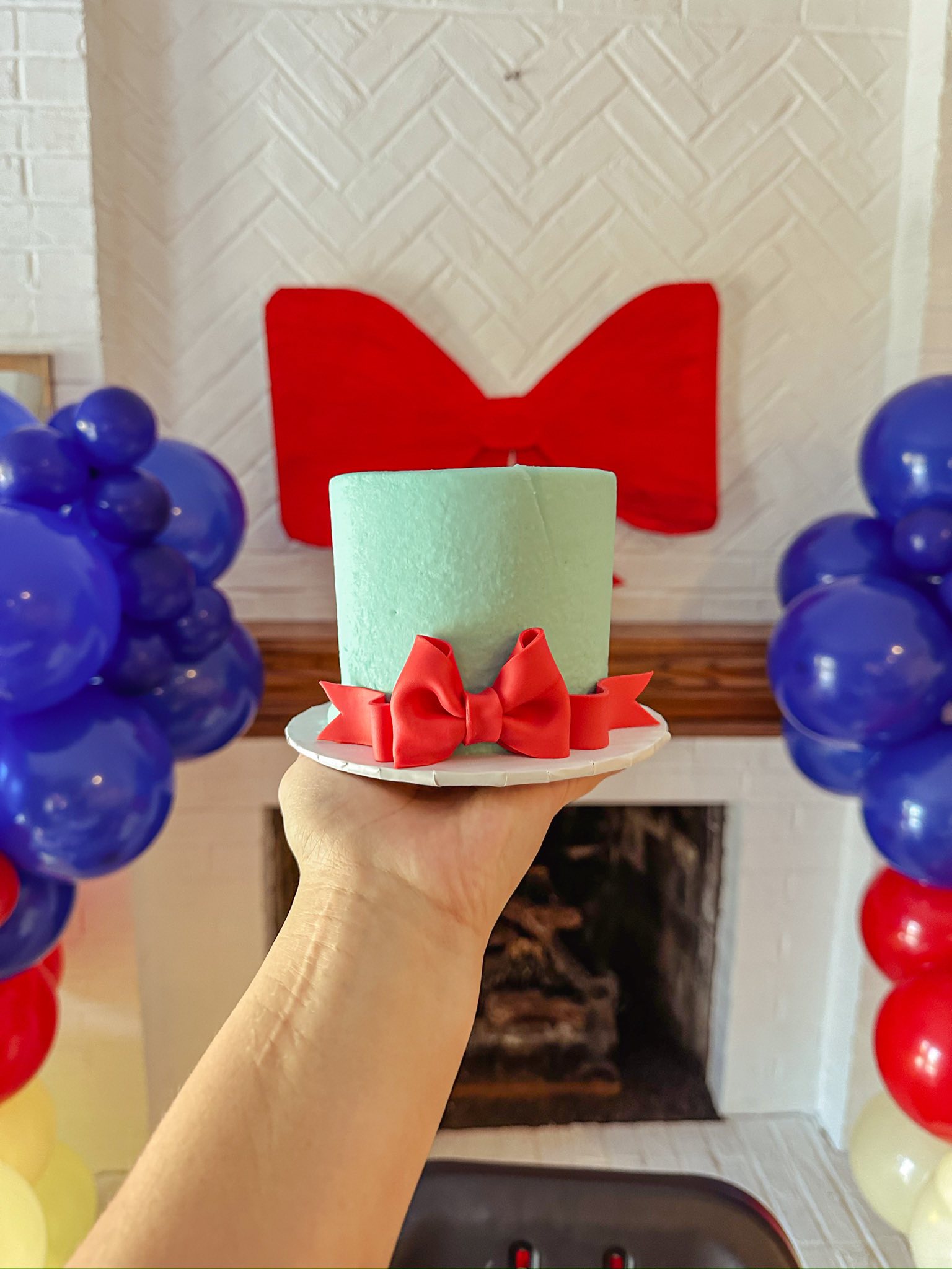 Mint green smash cake with a red fondant bow held in front of a fireplace with red, white, and blue balloons.