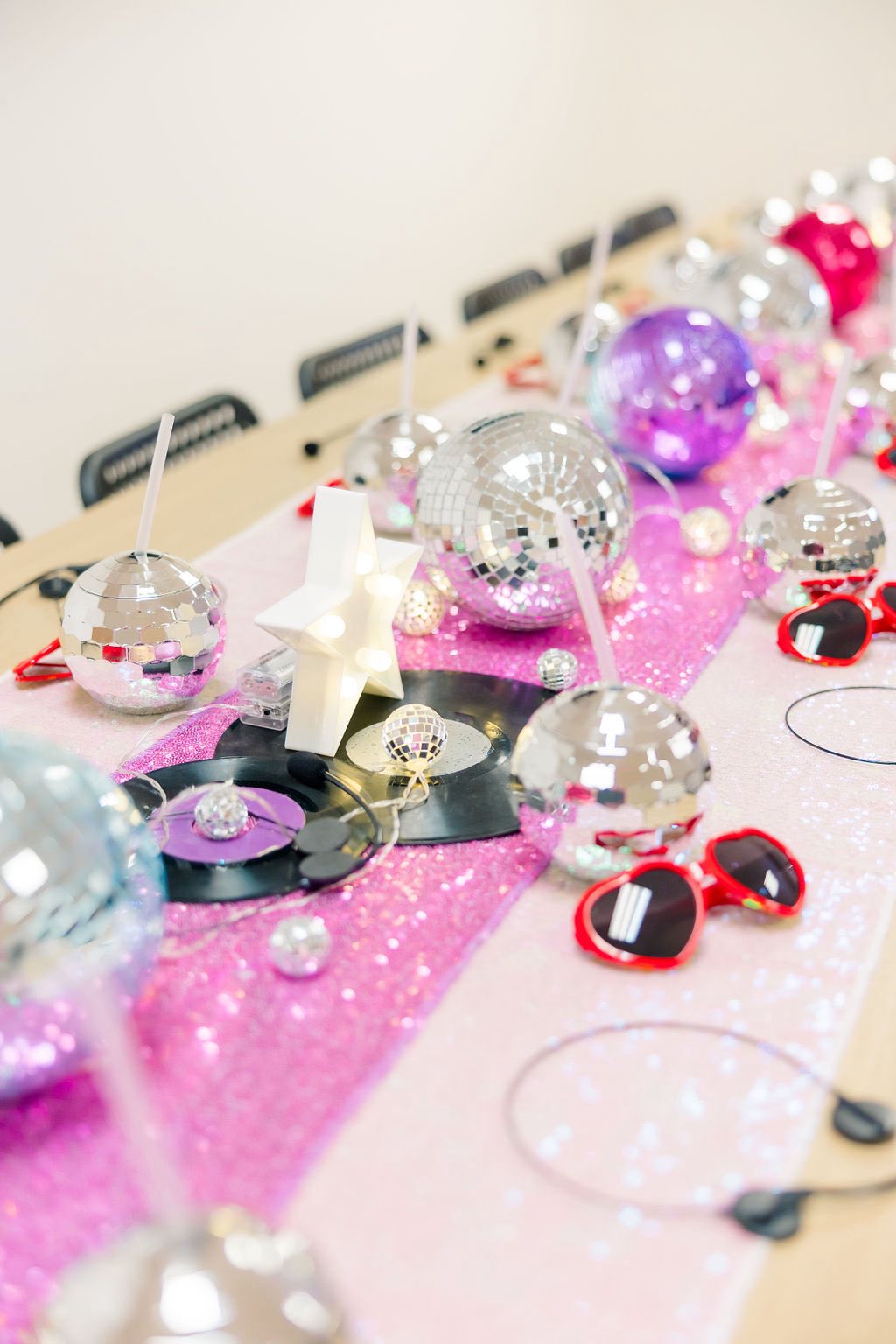 Table setting with mirror disco ball cups, light-up star decor, vinyl records, and heart-shaped sunglasses on pink.