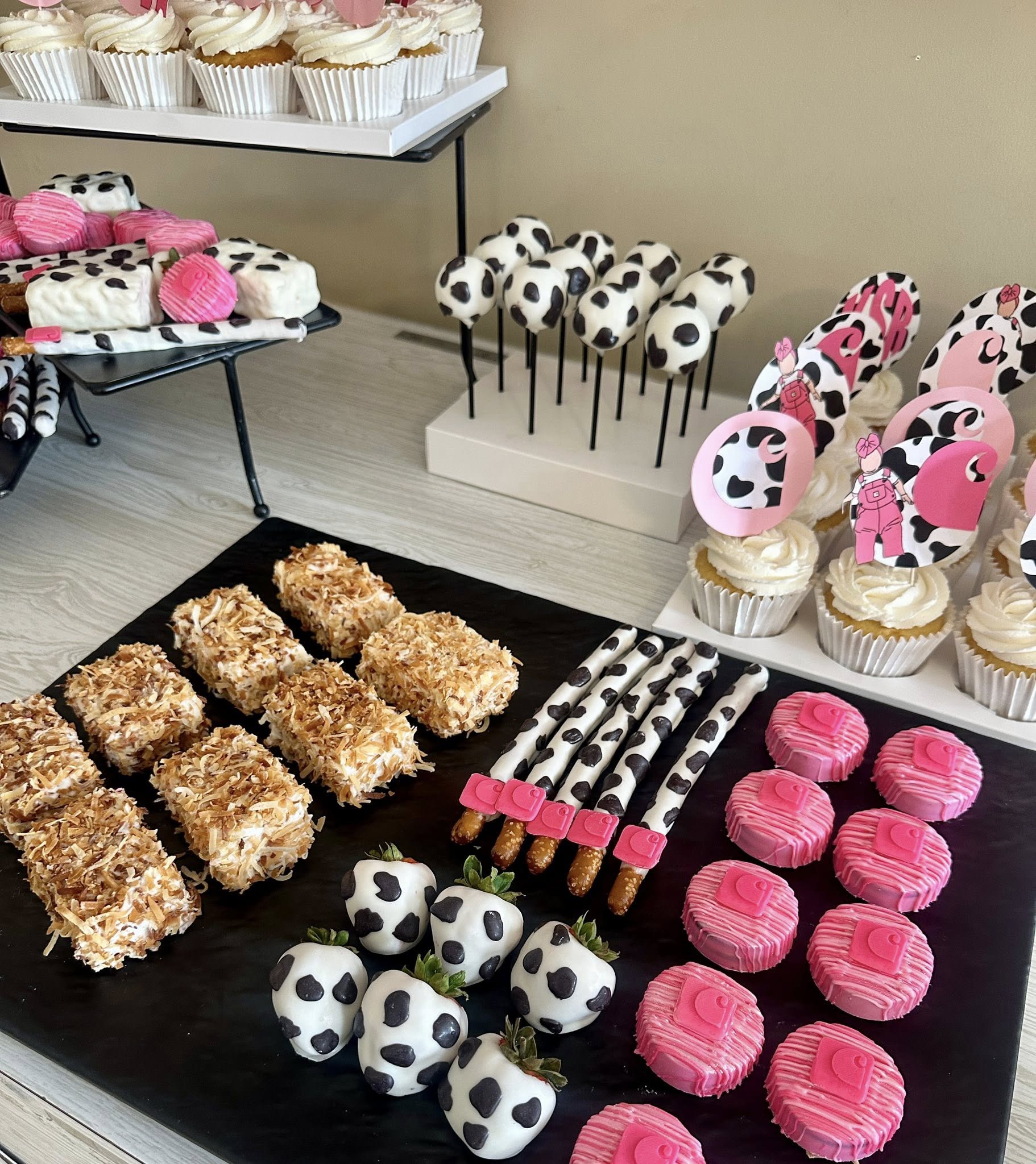Table display of cow print theme desserts including chocolate covered strawberries, pretzels, and pink frosted treats.