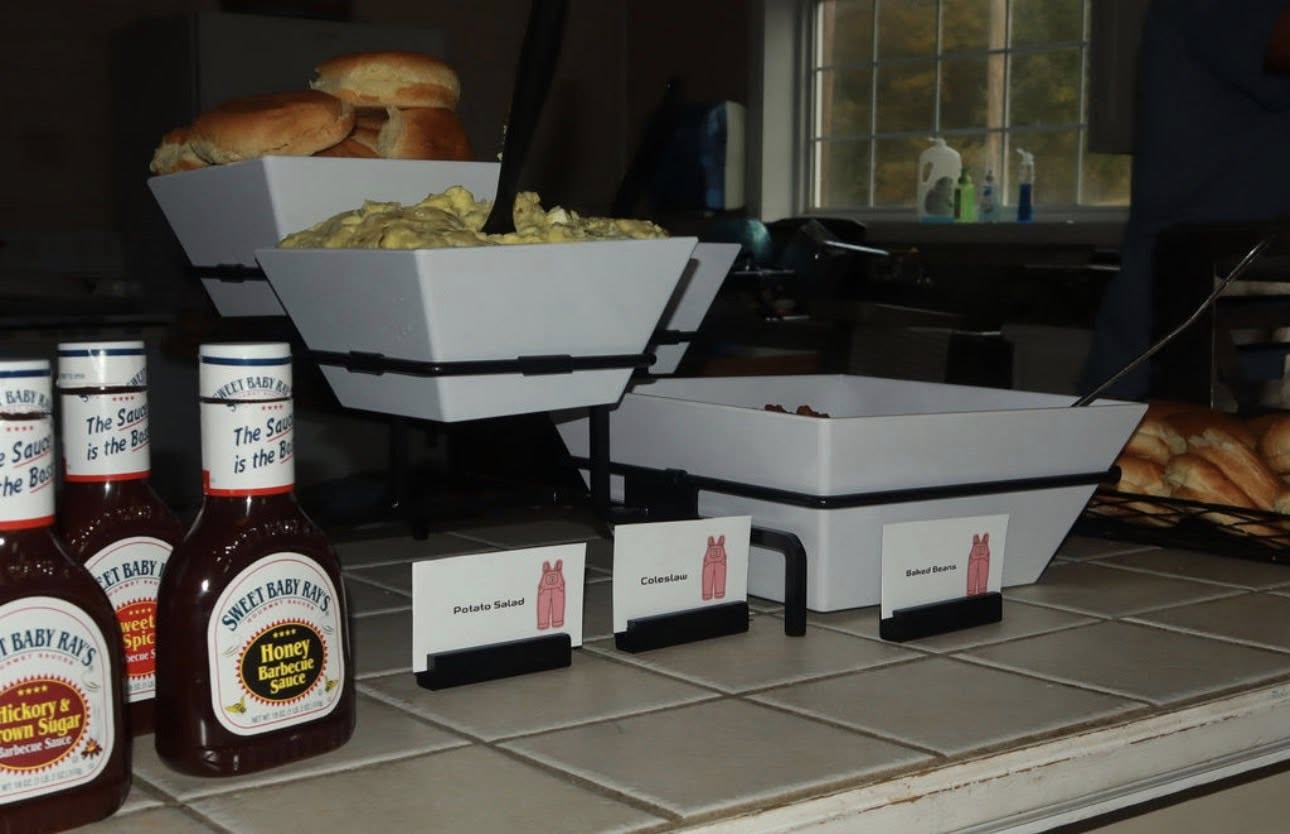 Table spread featuring Sweet Baby Ray's barbecue sauce, potato salad, coleslaw, and baked beans with bread rolls.