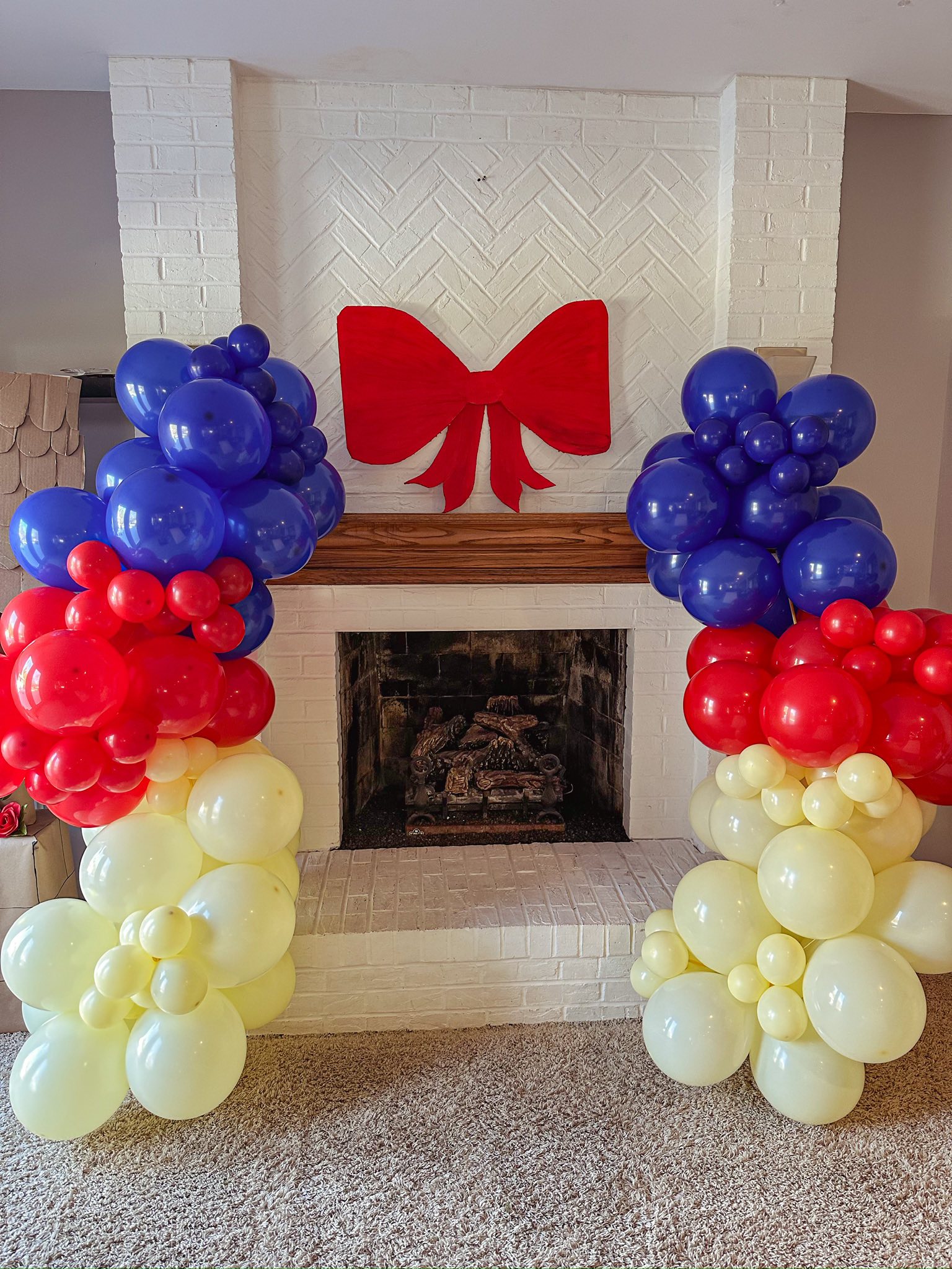 Fireplace decorated with red, blue, and yellow balloon pillars and a large red bow on the mantel