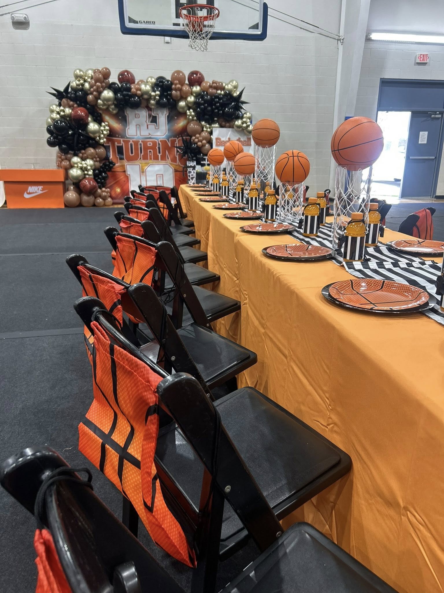 Basketball themed party table setup with orange basketball plates, miniature hoops, and orange chair covers.