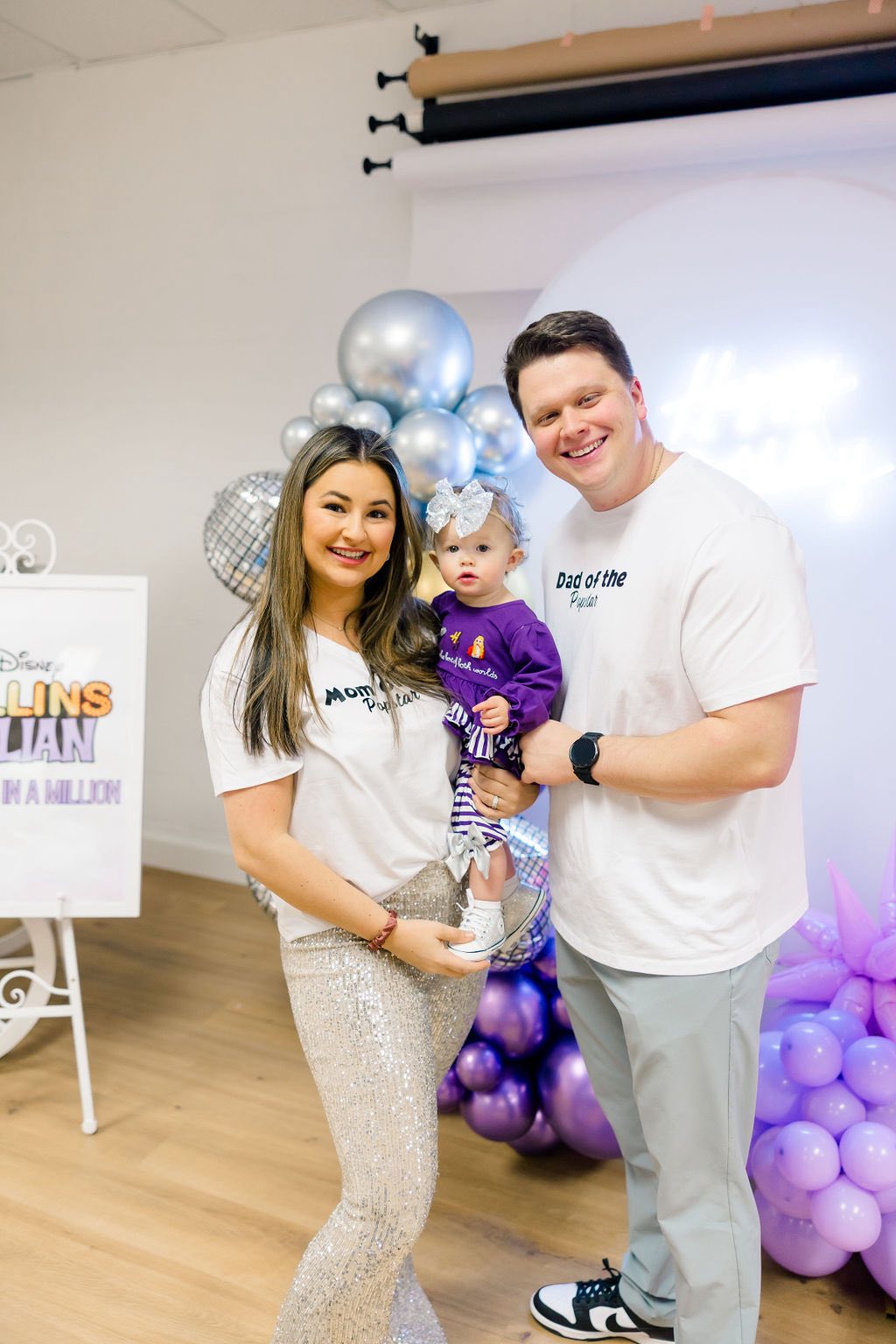 Family posing in coordinated Mom Popstar and Dad of the Popstar t-shirts with their daughter at a party.