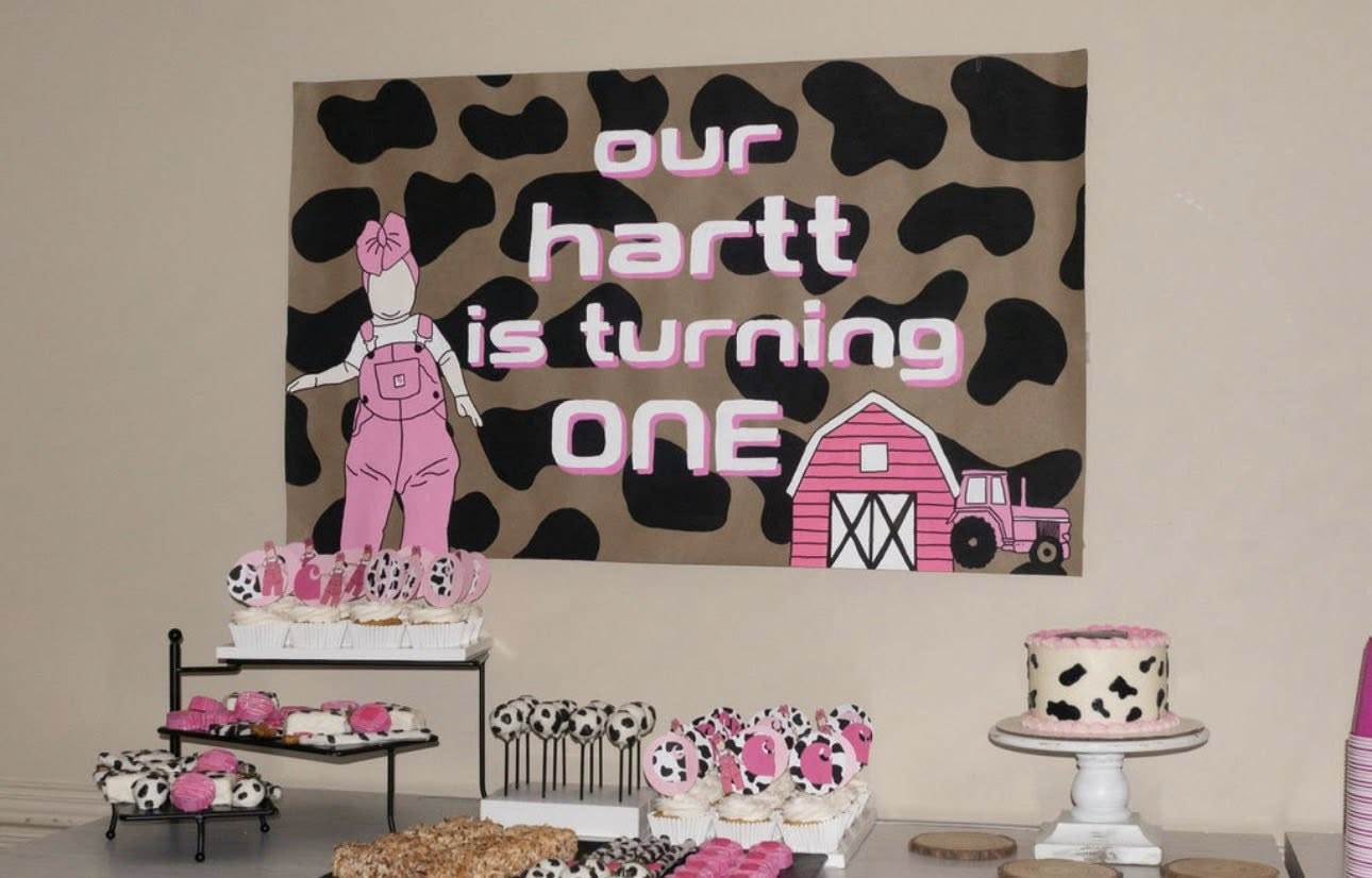 First birthday party banner with cow print background, pink barn, and matching cow themed desserts