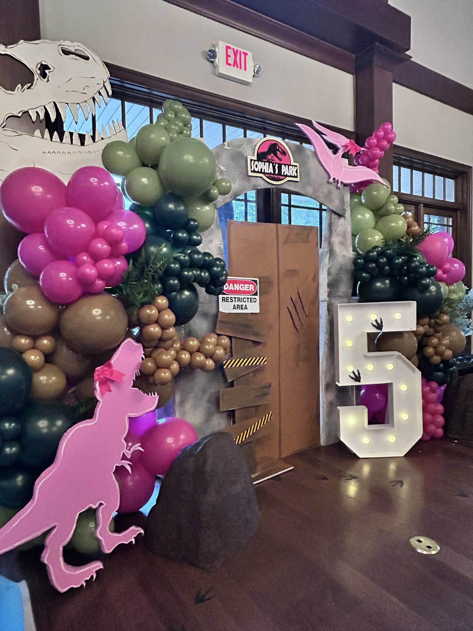 Dinosaur-themed birthday decoration with balloons, a Sophia's Park sign, and a large light-up number 5.