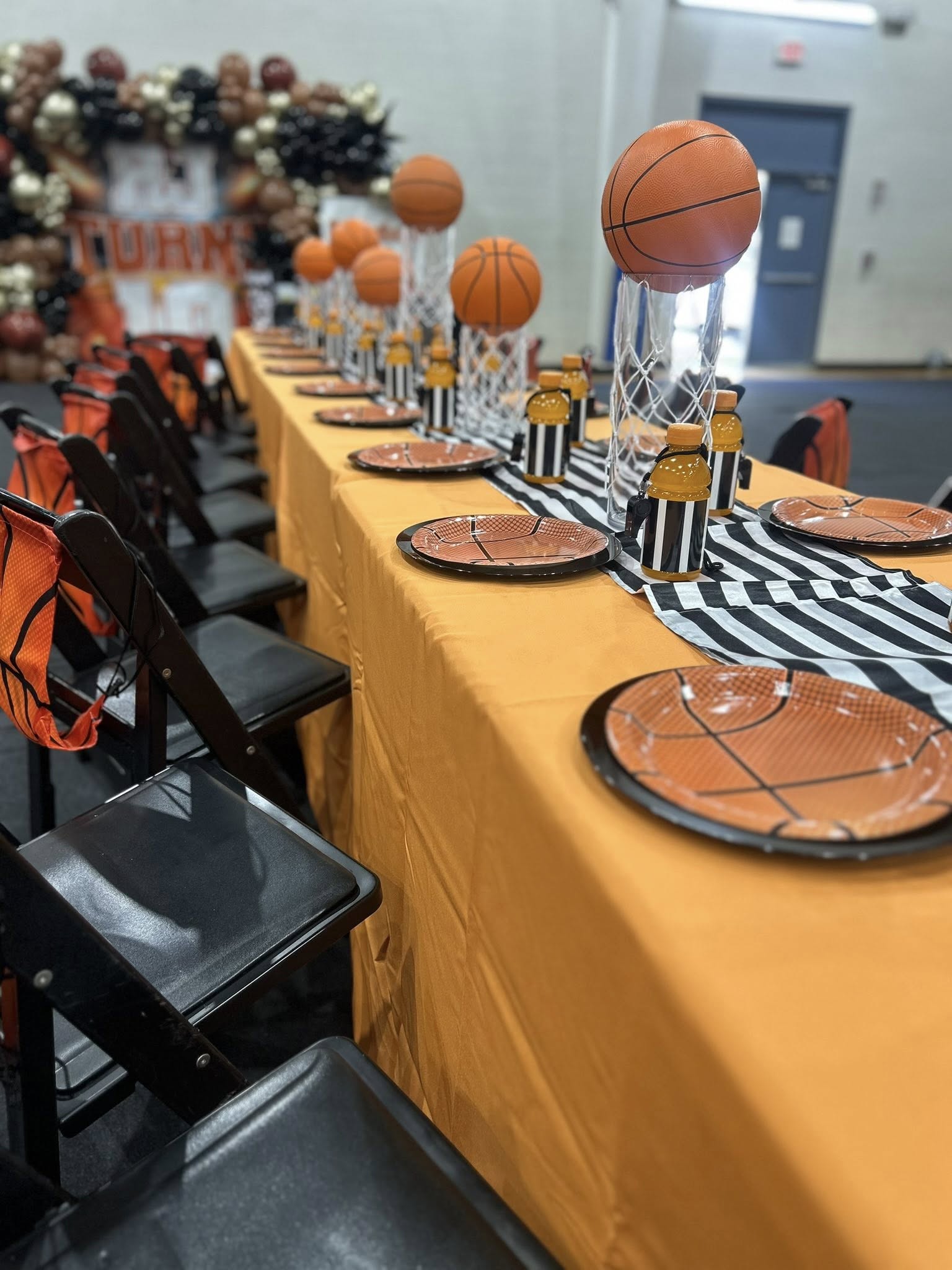 Table set for a basketball-themed party with basketball centerpieces, orange tablecloth, and basketball plates.
