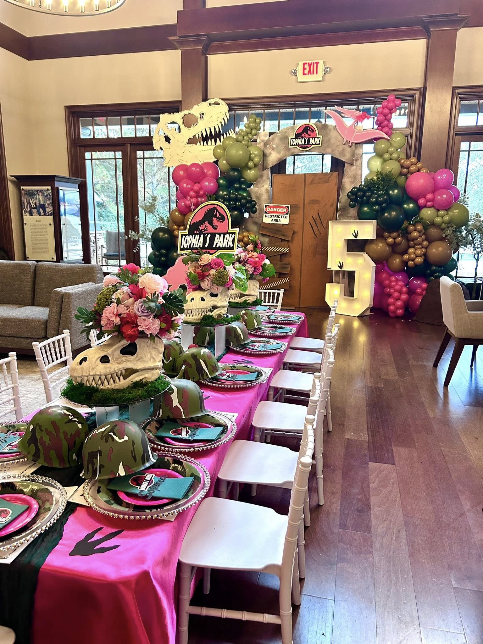 Dinosaur-themed birthday party setup with skull centerpieces, camo helmets, and a large light-up number five