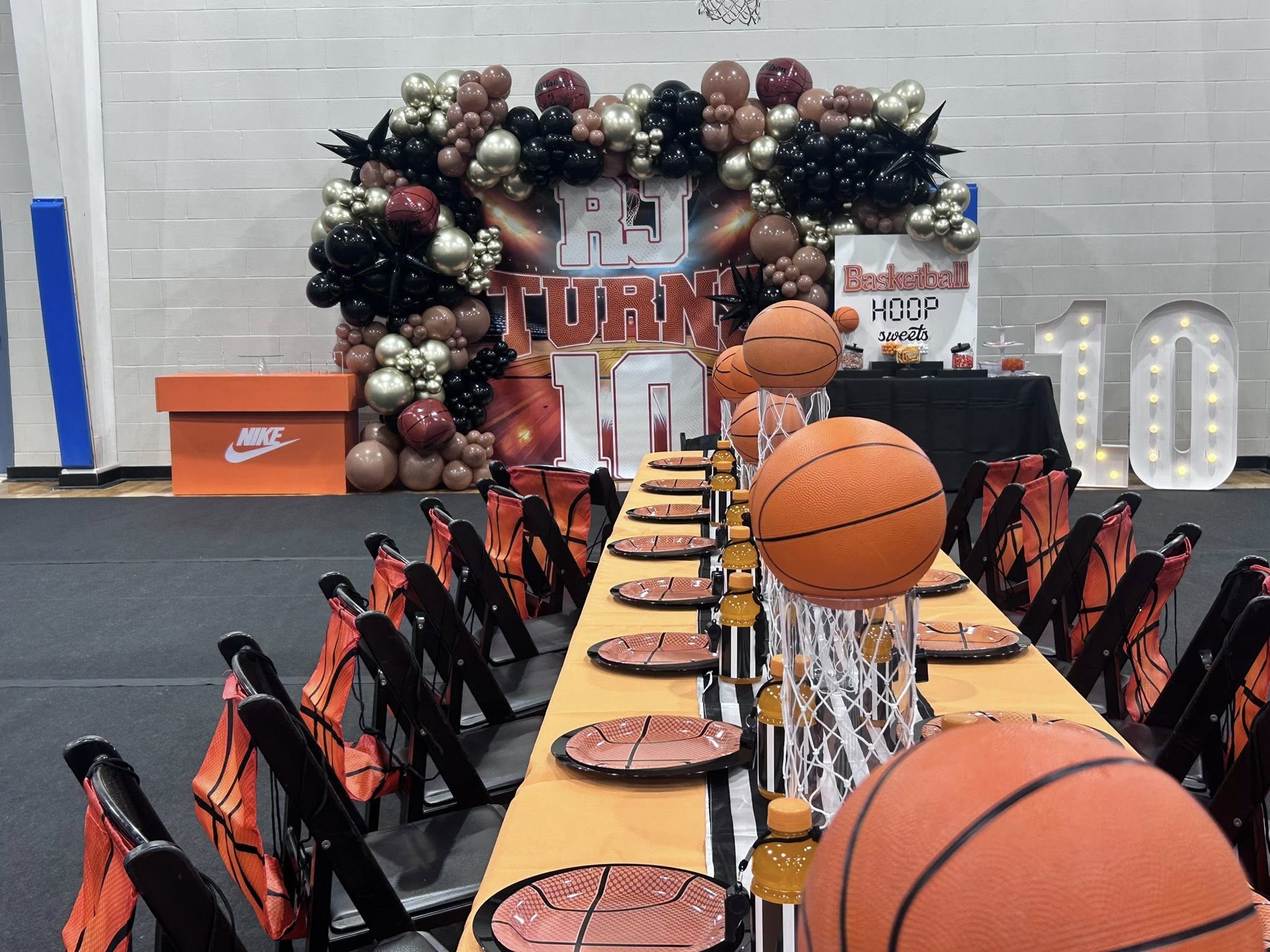 Basketball-themed party setup with balloon arch, orange plates, and table decorations including mini basketball hoops.