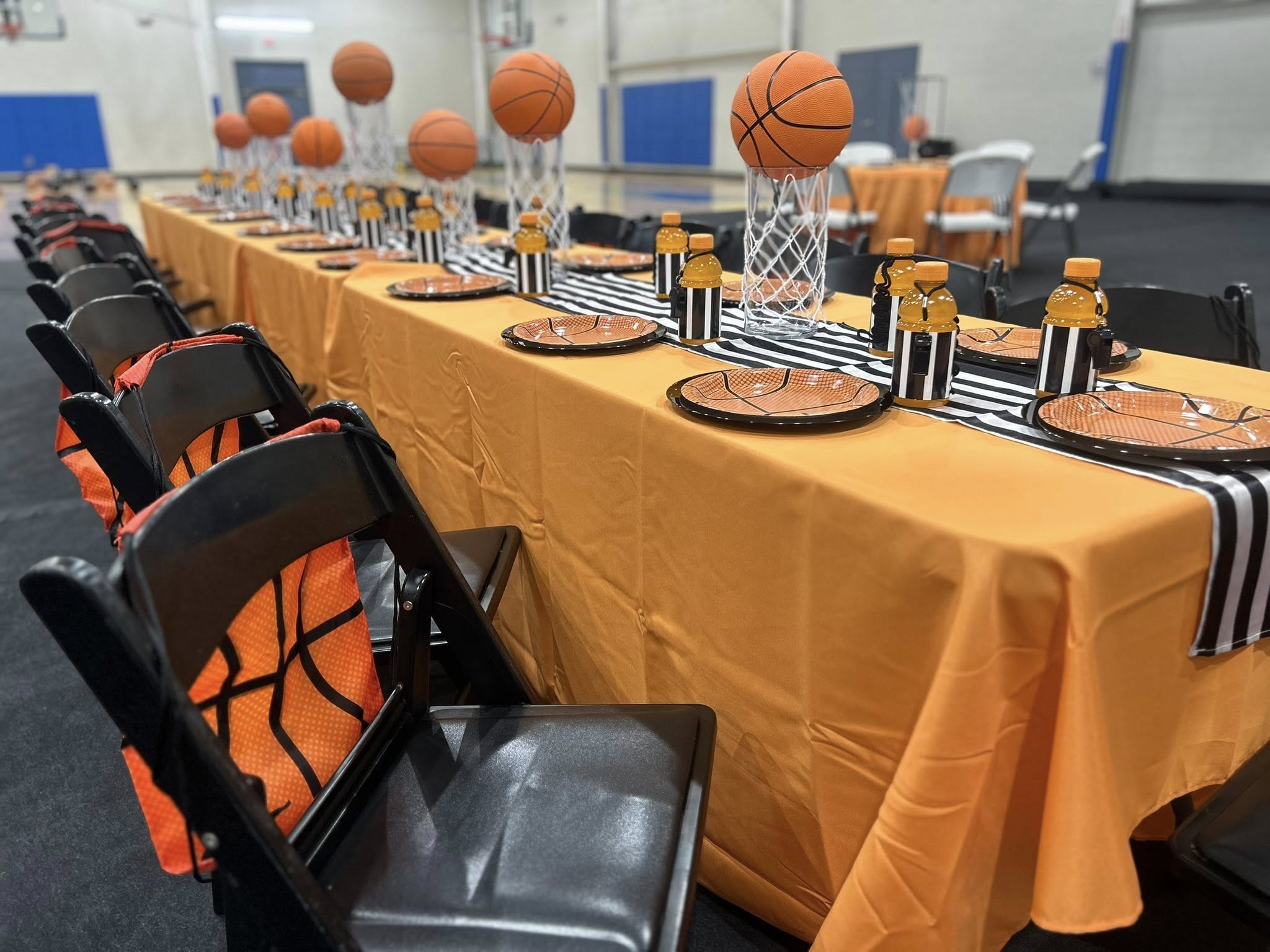 Basketball themed party table setting with orange tablecloths, basketball plates, and centerpieces.