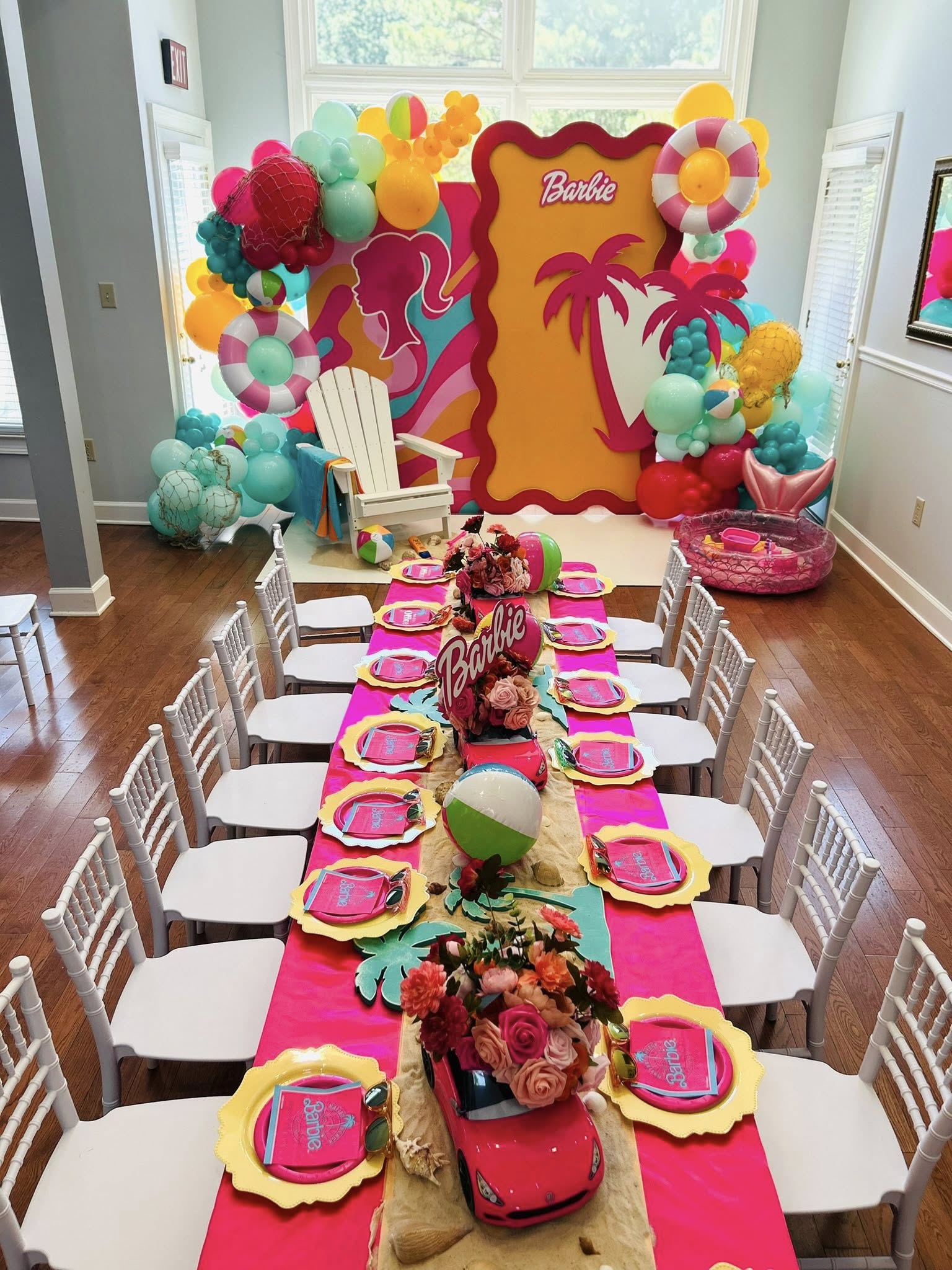 Barbie themed beach party table setup with pink runner, floral centerpieces, and decorative balloon backdrop.