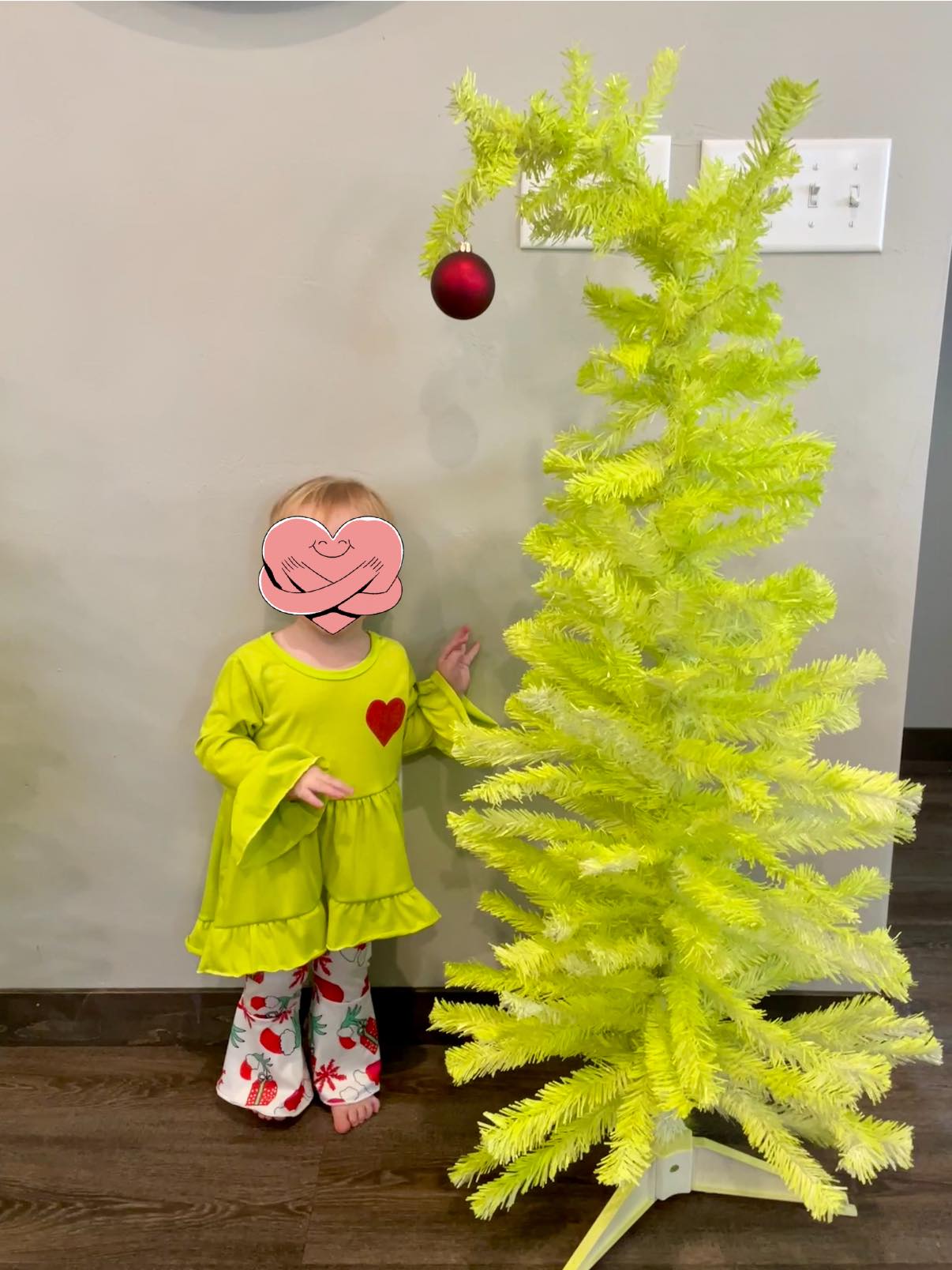 Toddler wearing a lime green bell-sleeve top with a red heart and patterned leggings standing next to a lime green Christmas tree.