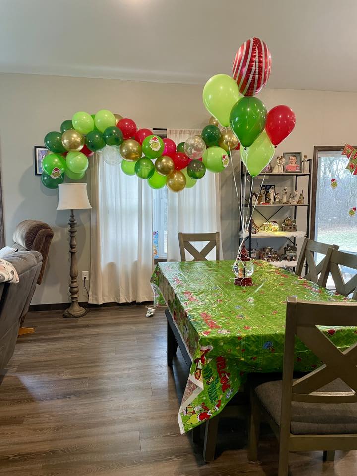 Dining room decorated with Grinch-themed green, red, and gold balloon arch and tablecloth