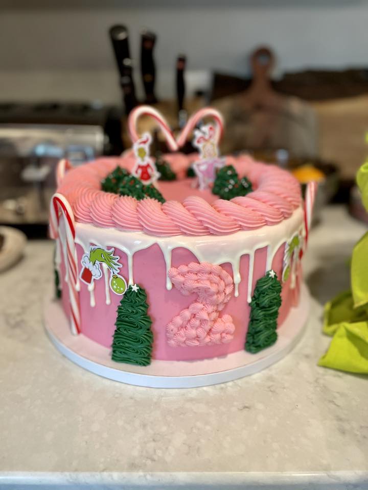 Two-tiered pink frosted Christmas cake with Grinch and candy cane decorations and a number two topper.