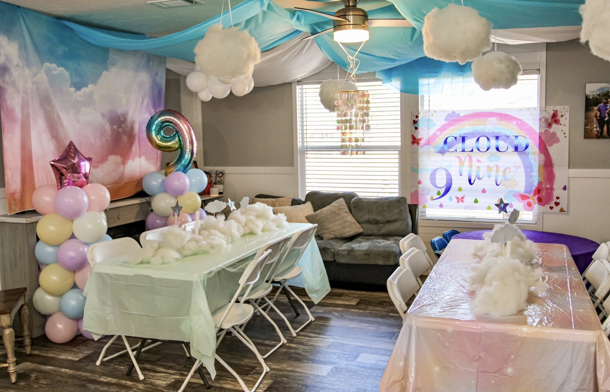 Cloud nine themed party decorations with rainbow banner, balloon arch, and clouds for a ninth birthday celebration.