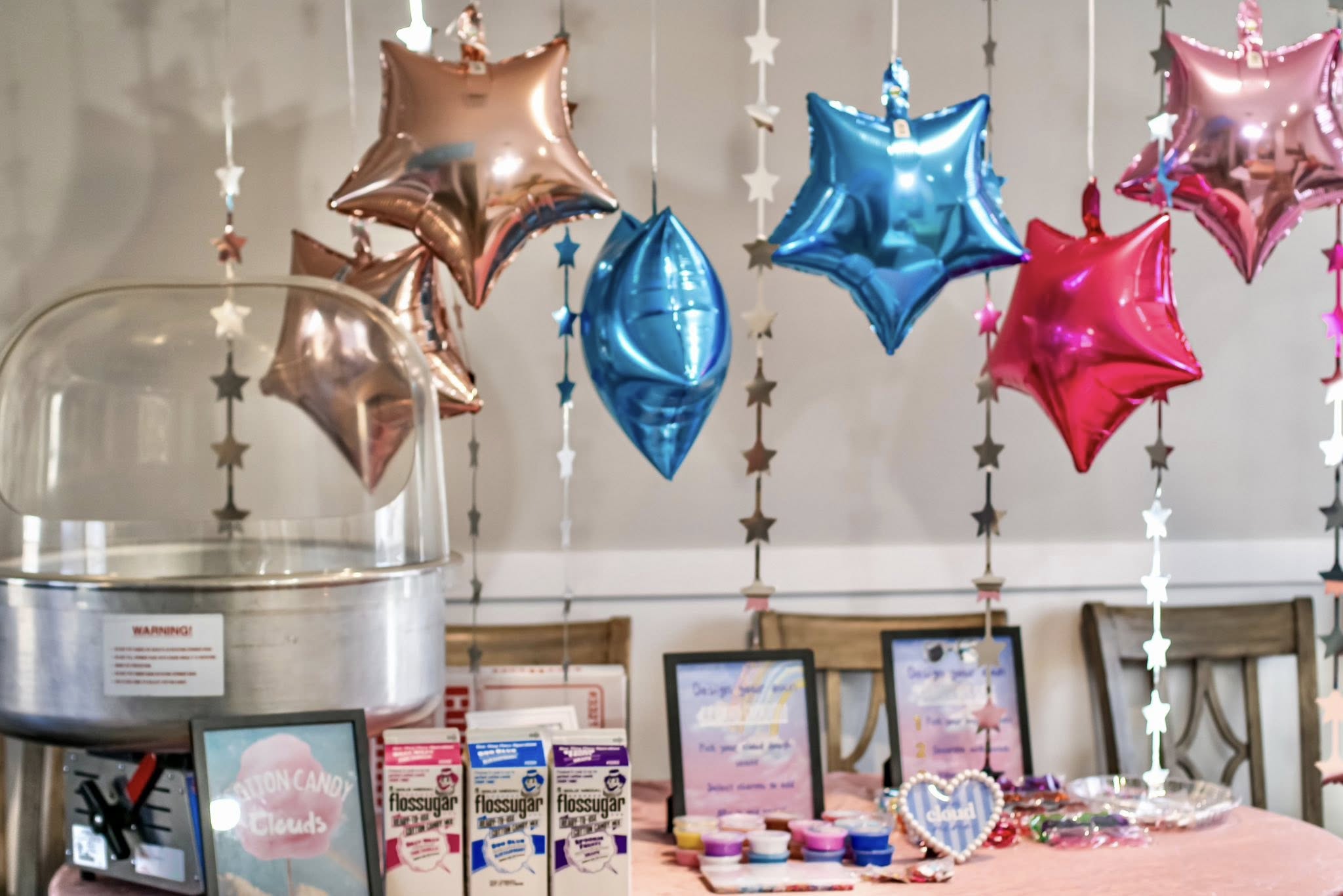 Table setup featuring cotton candy machine with party supplies, star balloons, and signage.