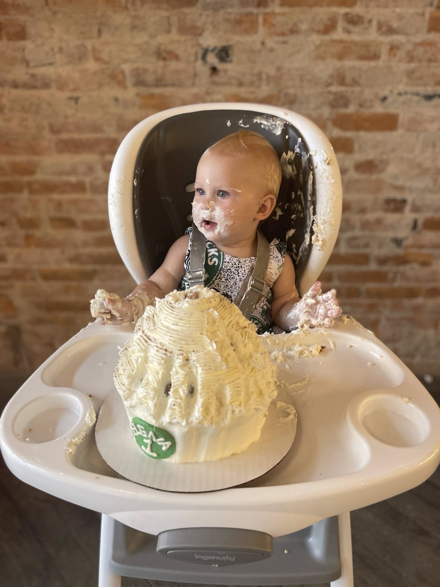 Toddler in a high chair covered in white cake during their first birthday cake smash