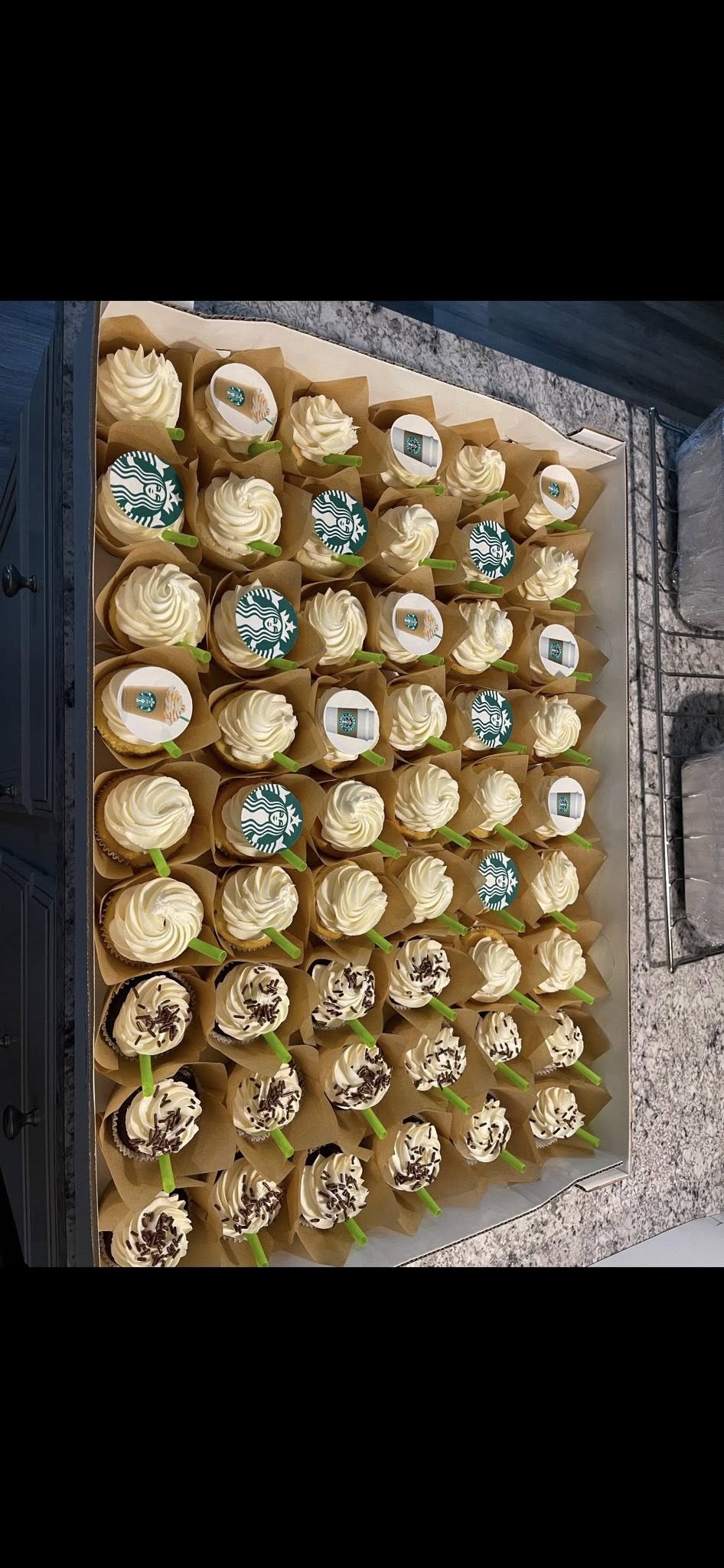 Box of assorted Starbucks-themed cupcakes featuring coffee cup toppers and green straw decorations.