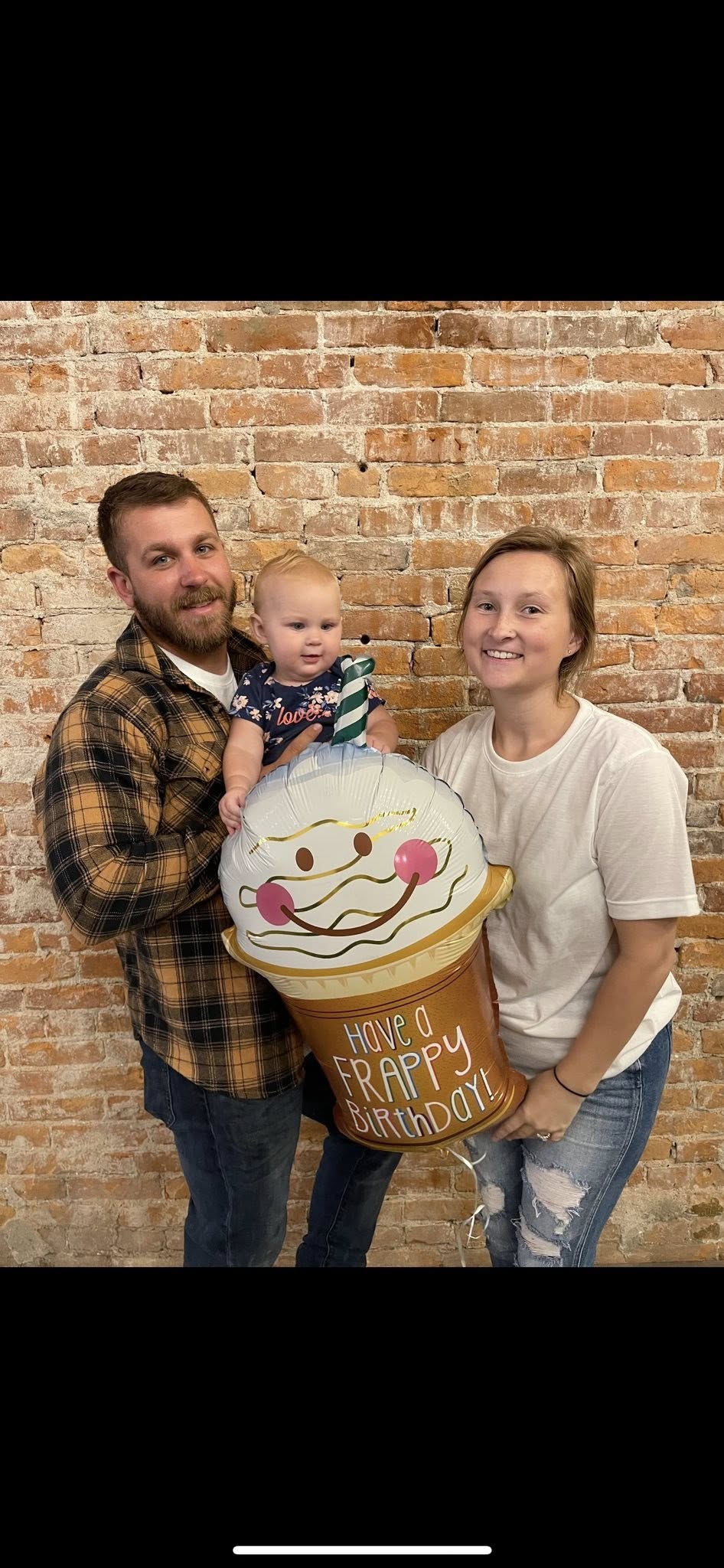 Family of three posing with a milkshake-shaped balloon that says Have a Frappy Birthday