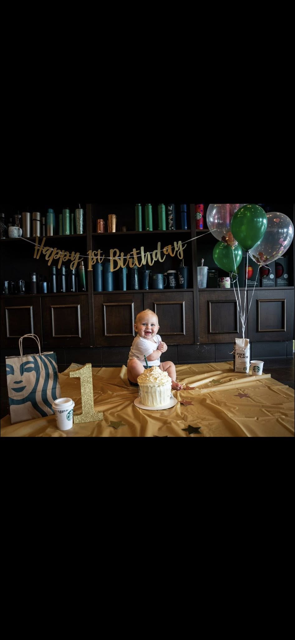 A baby sitting on the floor in front of a smash cake with a Happy 1st Birthday banner and balloons.