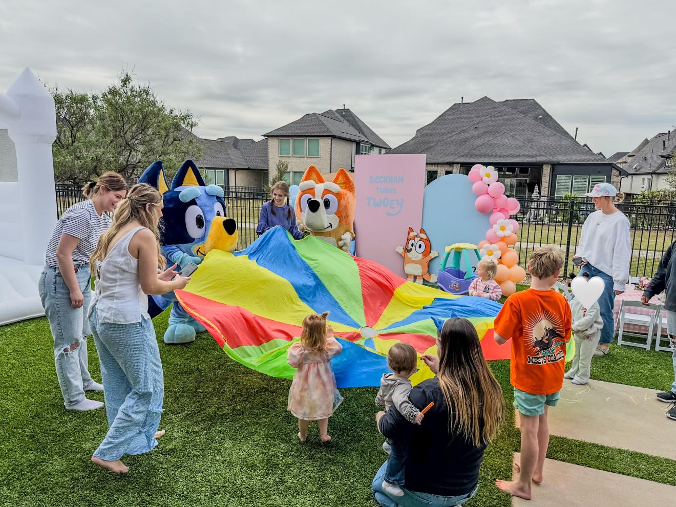 Children playing with a rainbow parachute at a Bluey-themed birthday party with character mascots