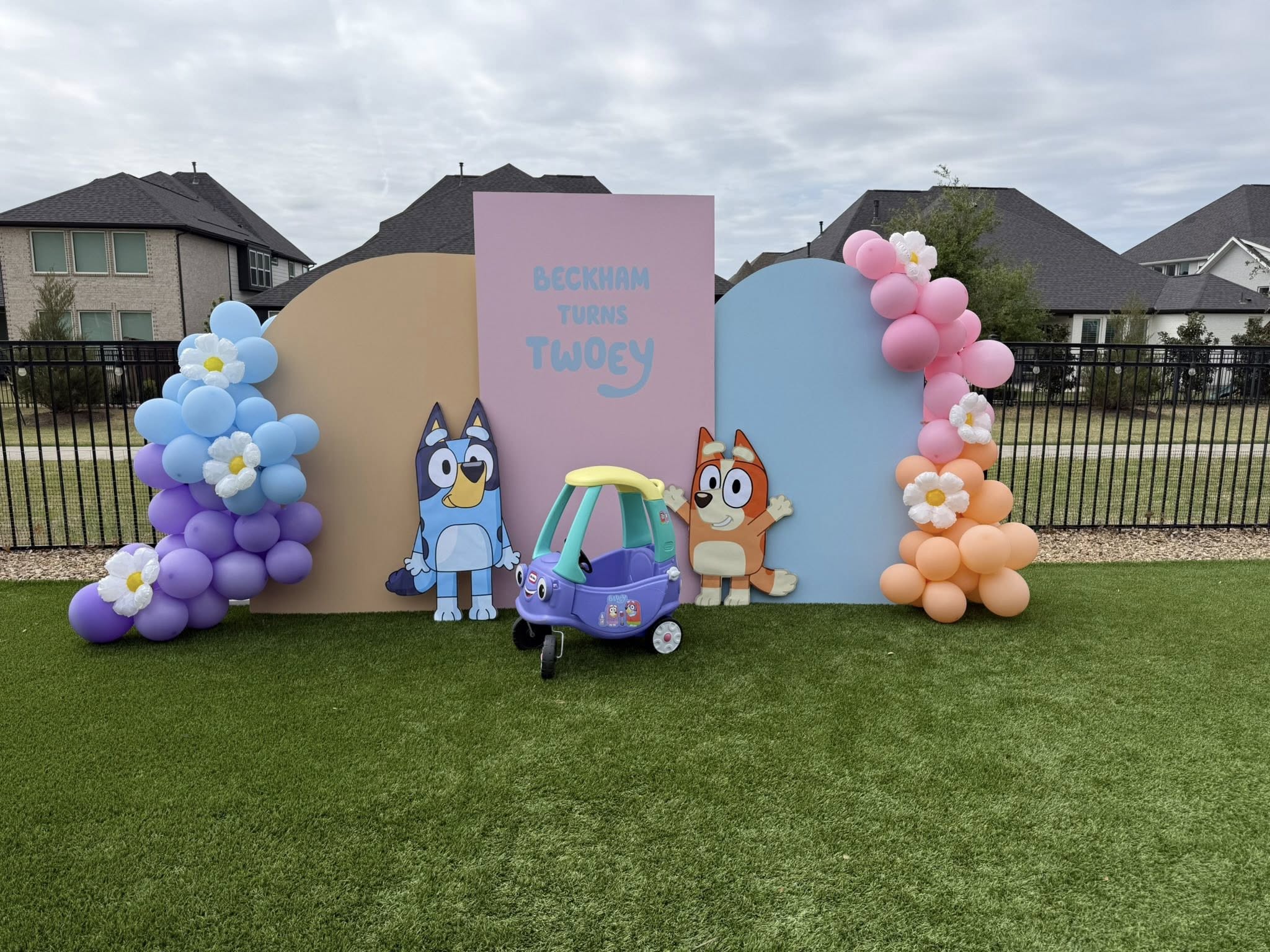 Colorful Bluey-themed second birthday party backdrop with arches, balloons, and a toy car.