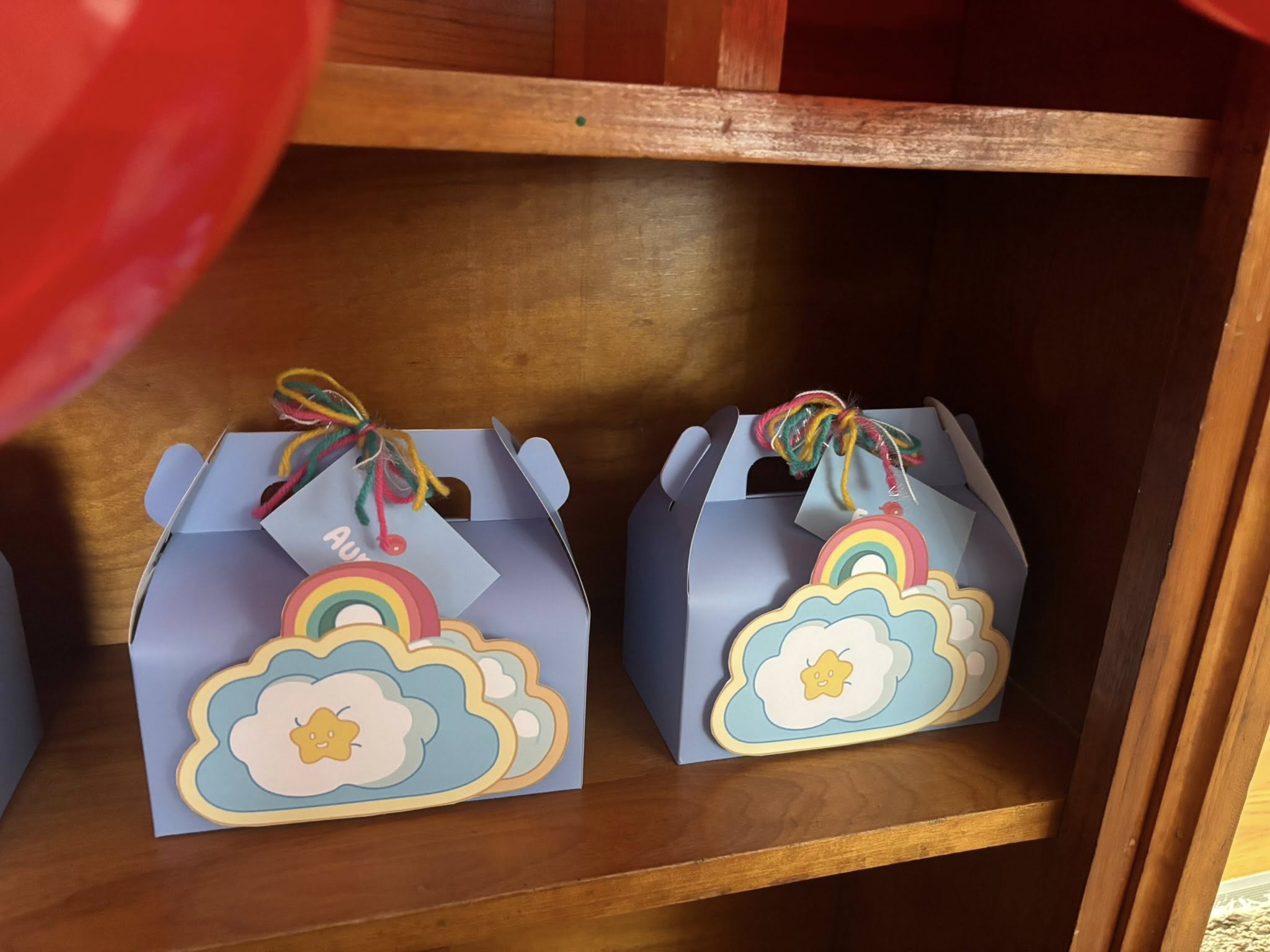 Two light blue gable party favor boxes decorated with rainbow and star cutouts, tied with multi-colored yarn.