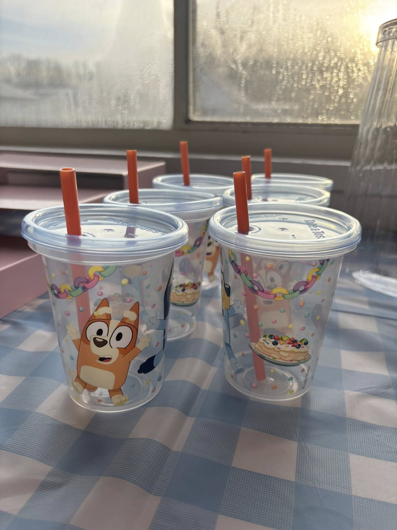 Set of clear plastic party cups featuring Bluey and Bingo with orange reusable straws.