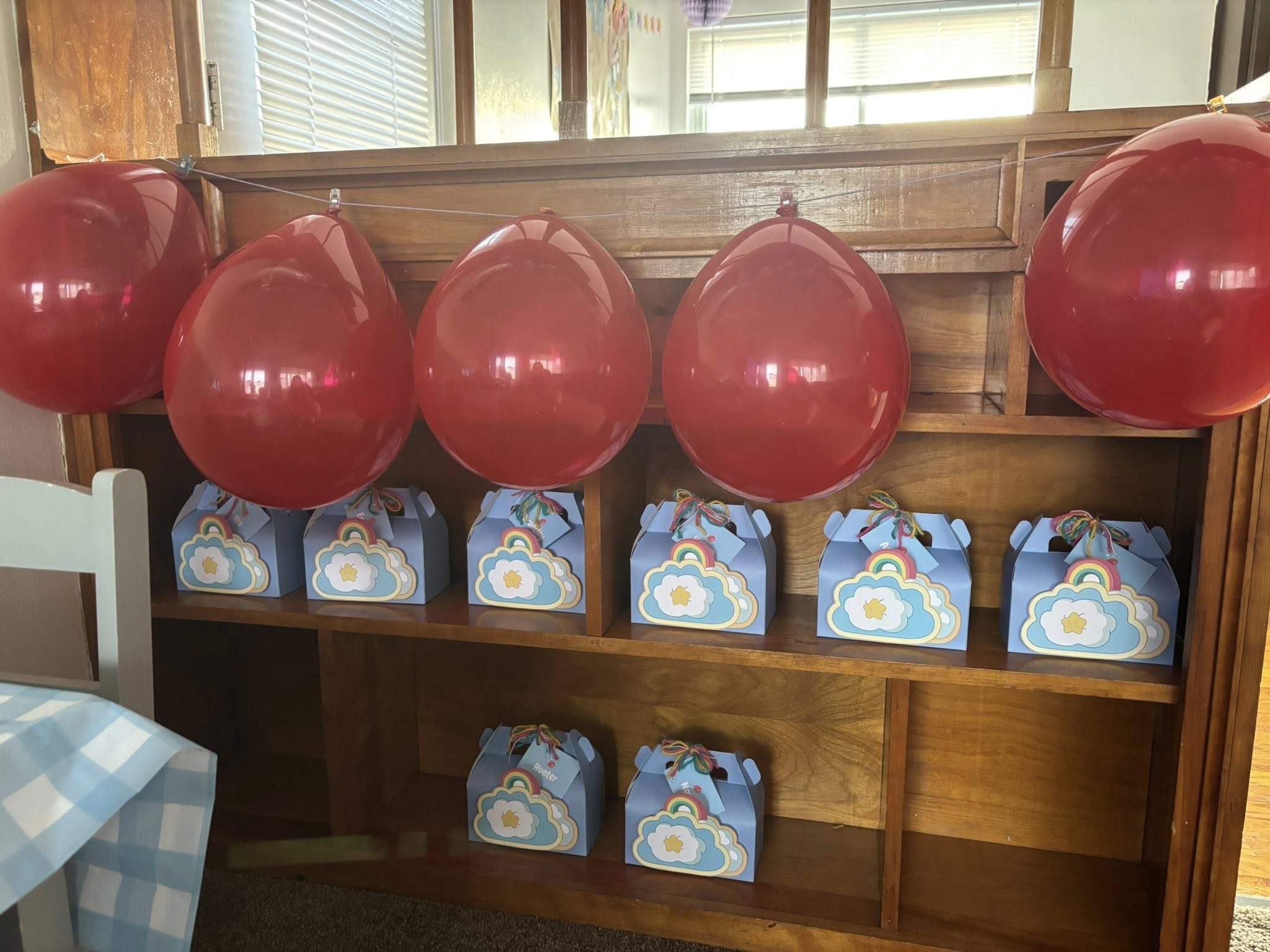 Blue gift boxes decorated with rainbow and cloud motifs displayed on a wooden shelf beneath red party balloons.