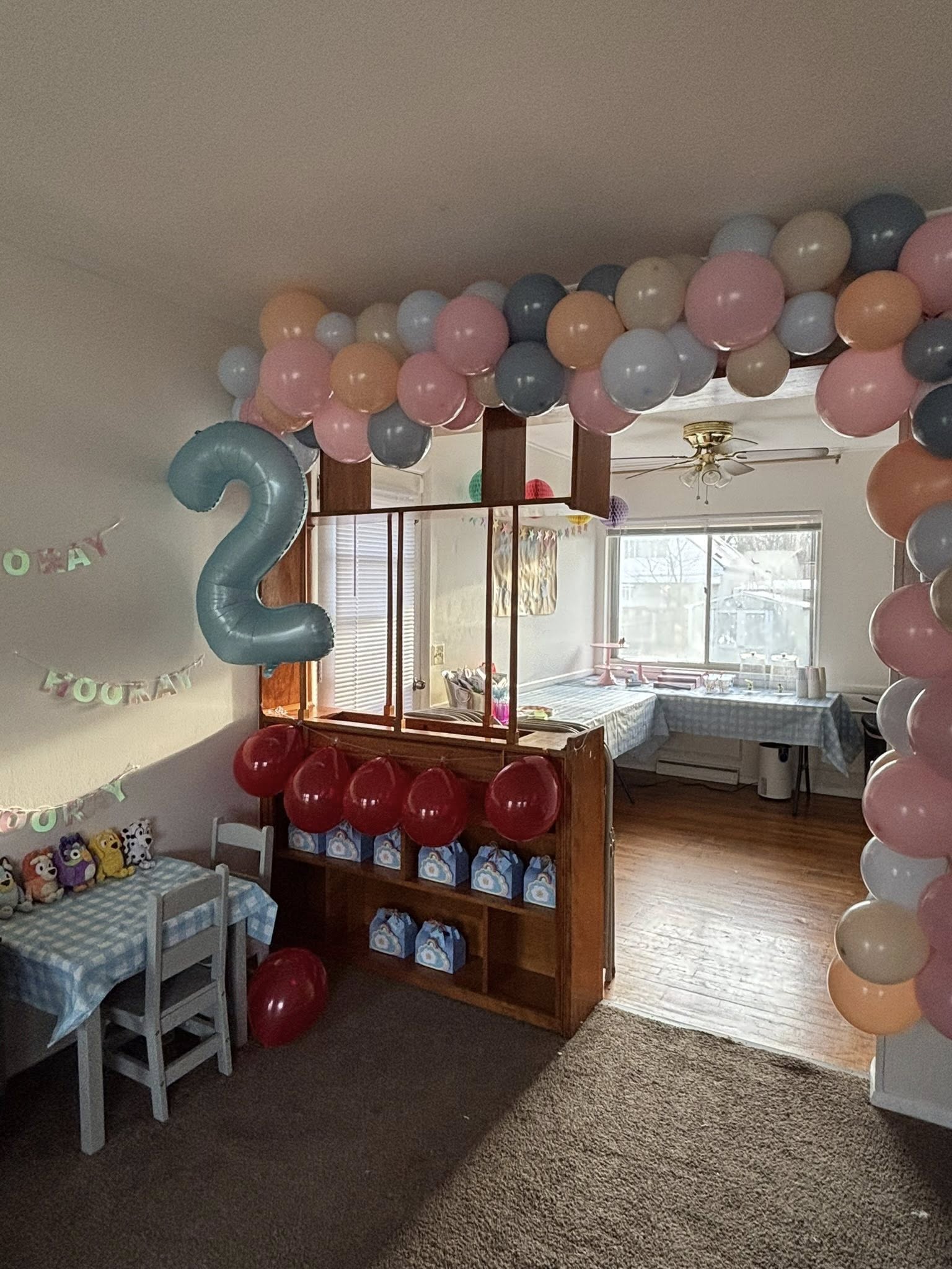 Living room decorated for a second birthday party with blue and pink balloons, a number two balloon, and party favors.
