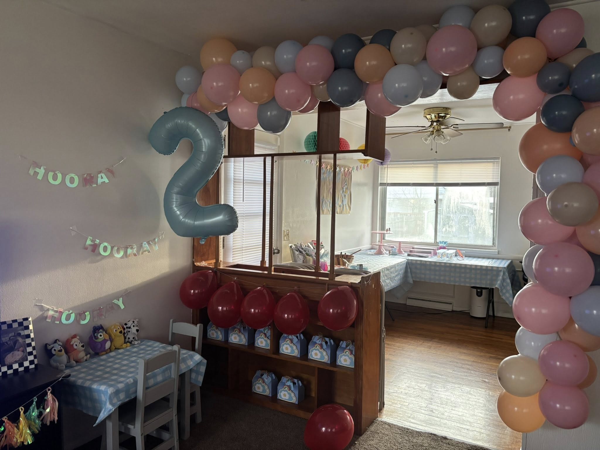 Living room decorated for a second birthday party with colorful balloon arches and a blue number two balloon.