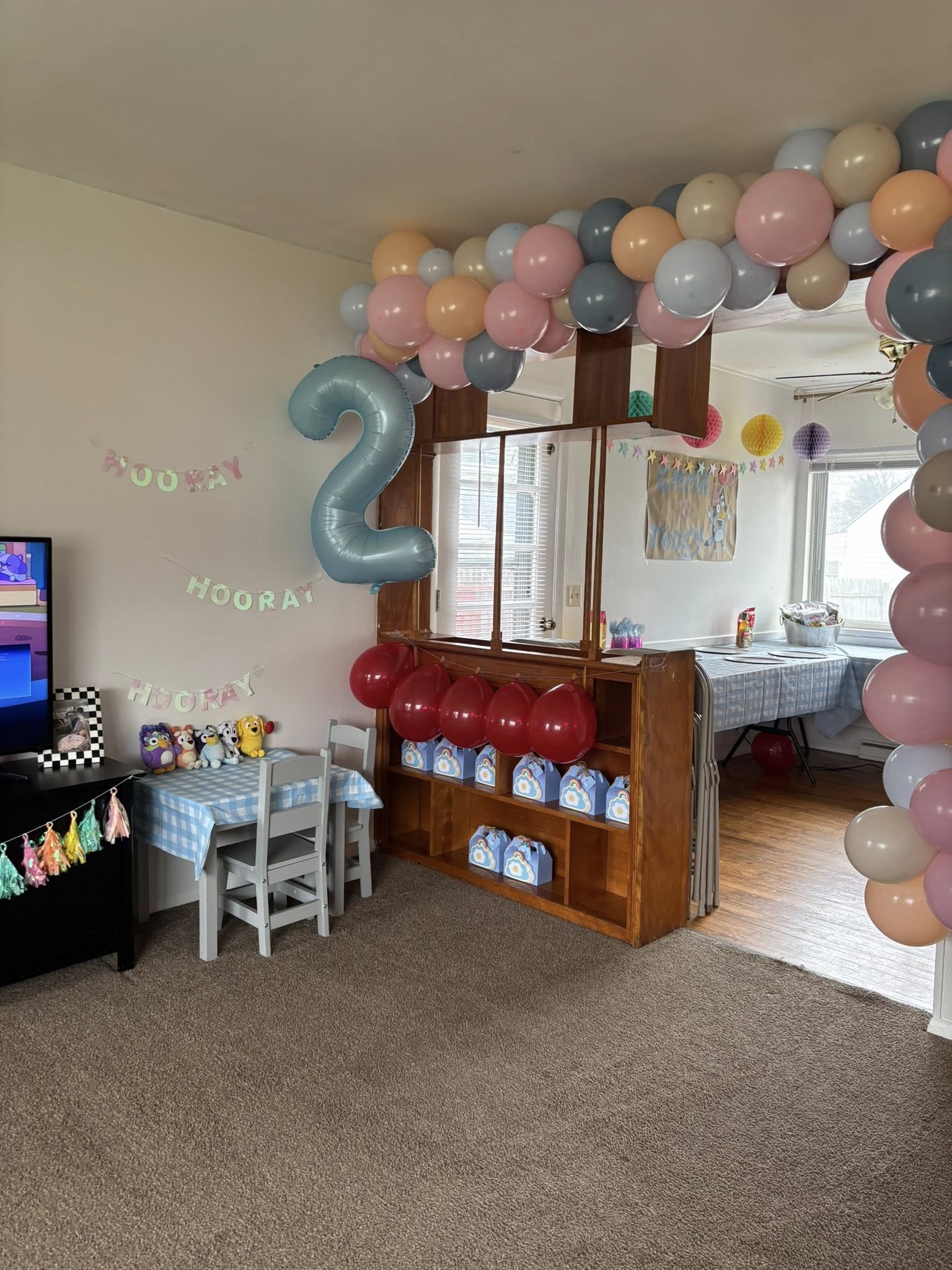 Living room decorated for a second birthday party with pastel balloons, a number two balloon, and party favors.