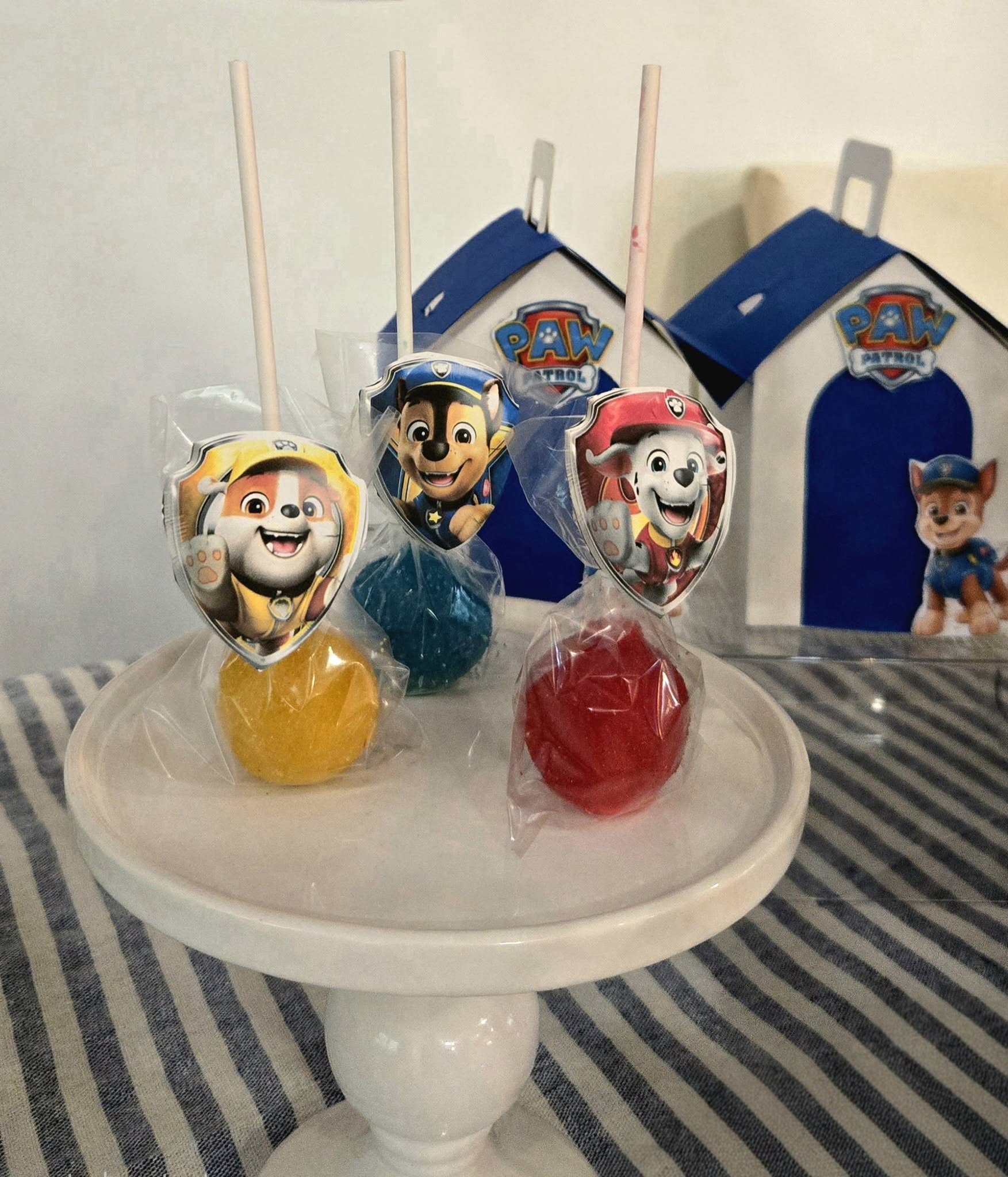 Paw Patrol themed round cake pops in yellow, blue, and red with character toppers on a white stand.