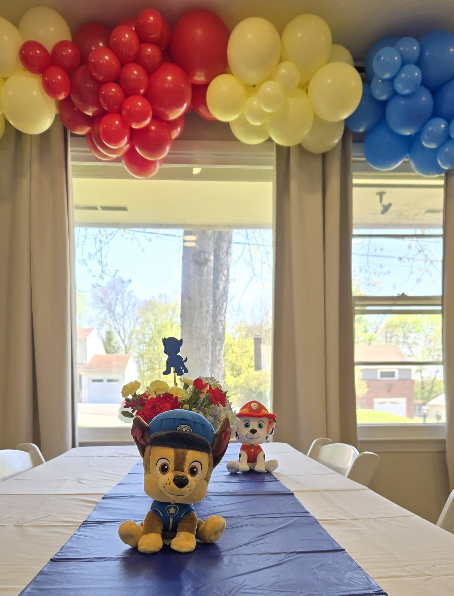 Paw Patrol theme table centerpiece featuring plush Chase and Marshall toys with a blue balloon arch overhead.