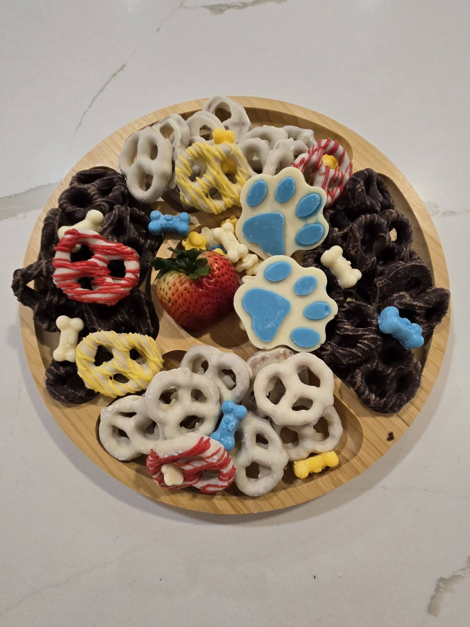 Wooden platter filled with chocolate-covered pretzels, candy paw prints, and a fresh strawberry