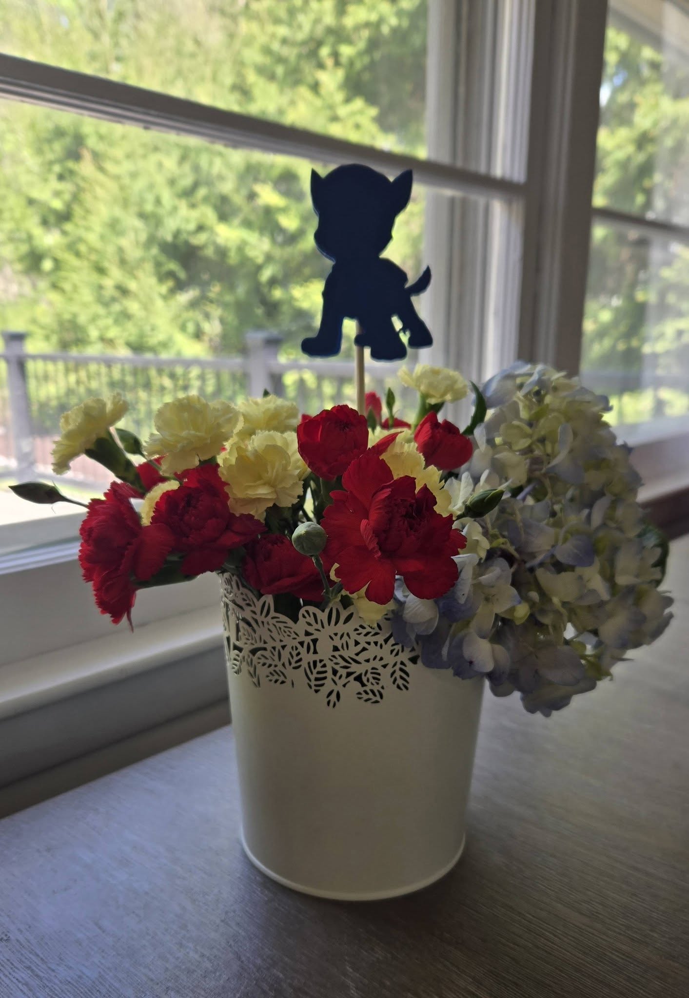 Table centerpiece featuring red and yellow carnations, blue hydrangeas, and a dark blue puppy silhouette topper.