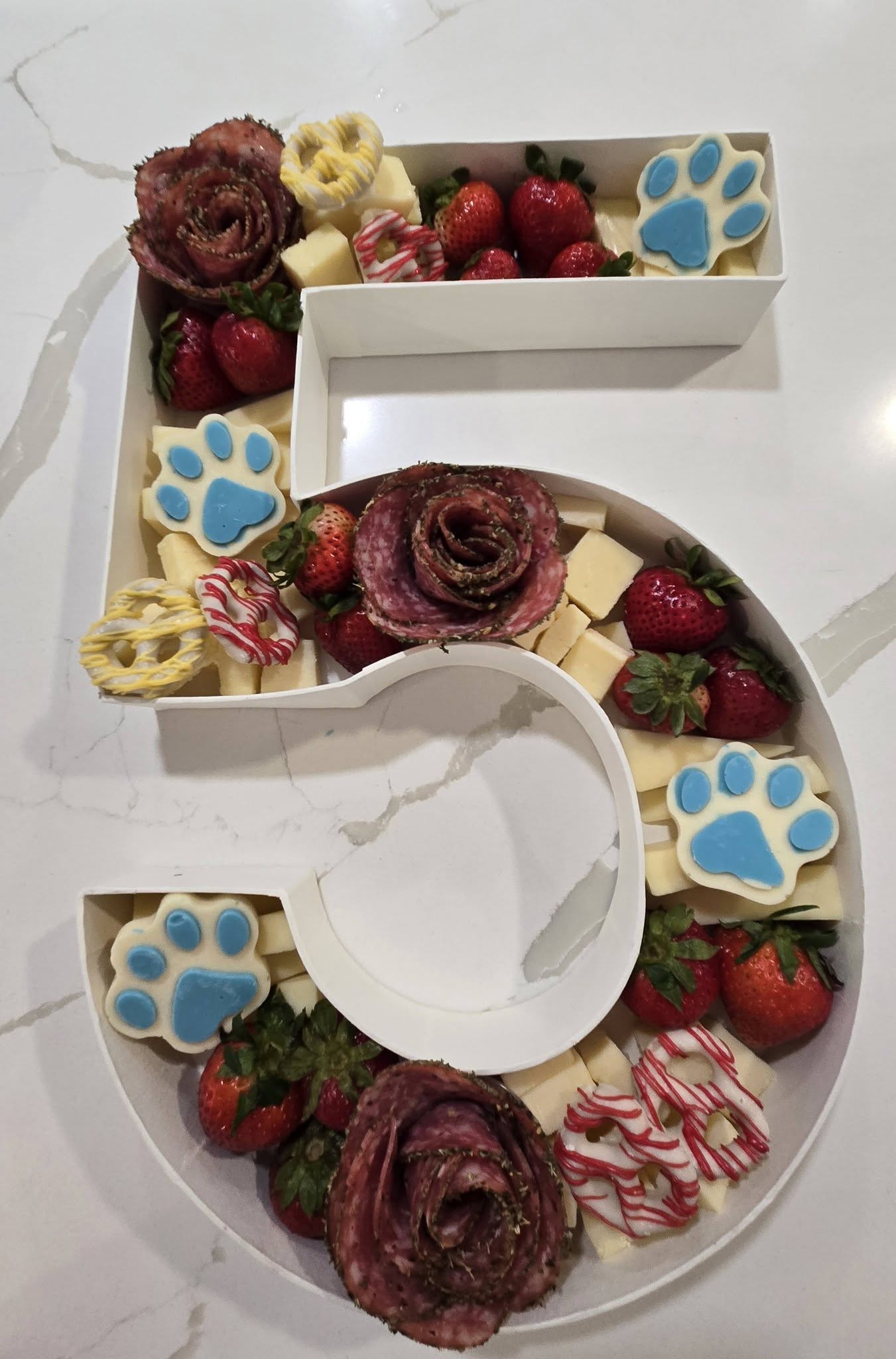 Number 5 shaped charcuterie board filled with salami roses, strawberries, cheese cubes, and paw print cookies.