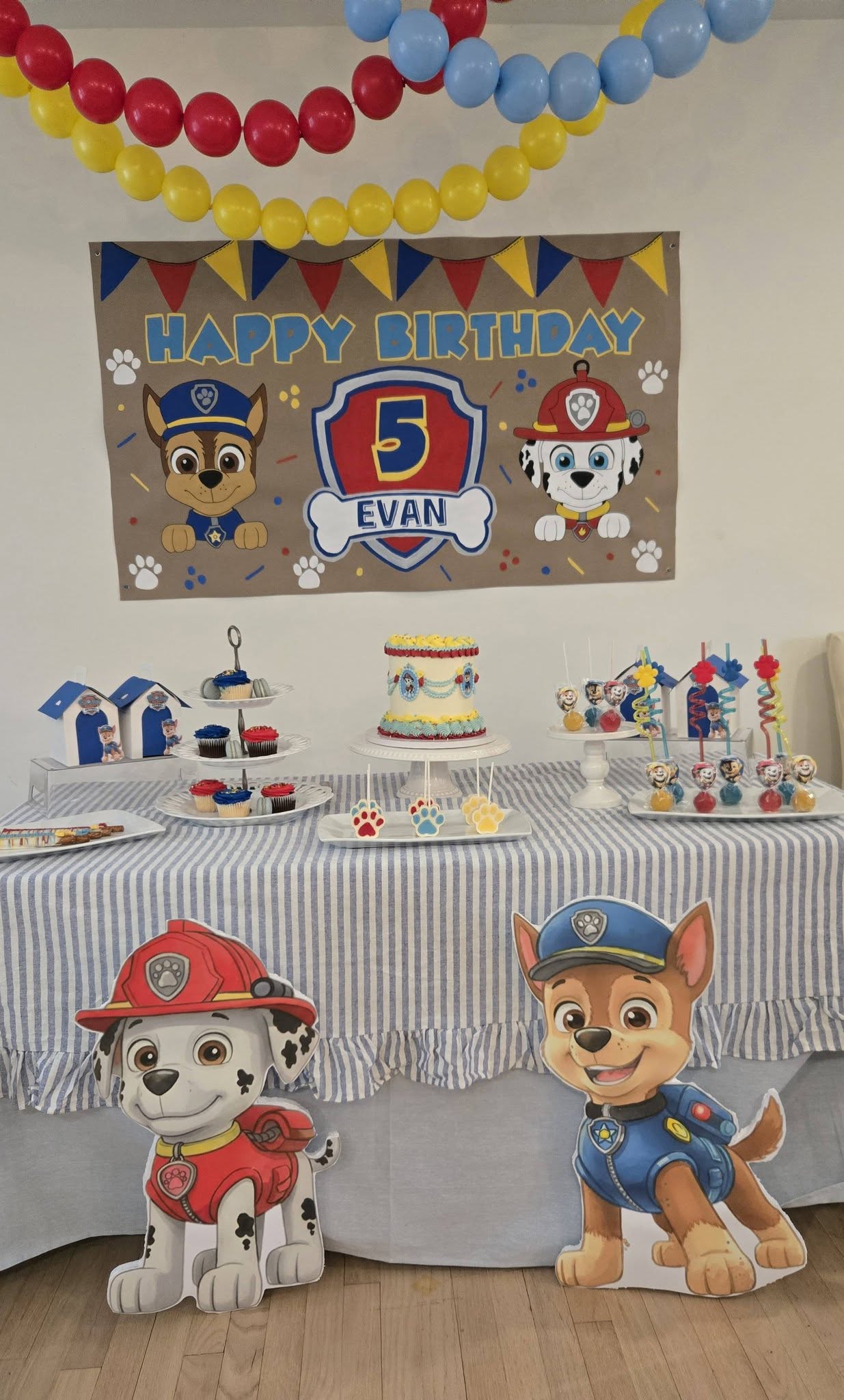 Paw Patrol themed 5th birthday party table with a personalized banner, cake, and cupcake display.