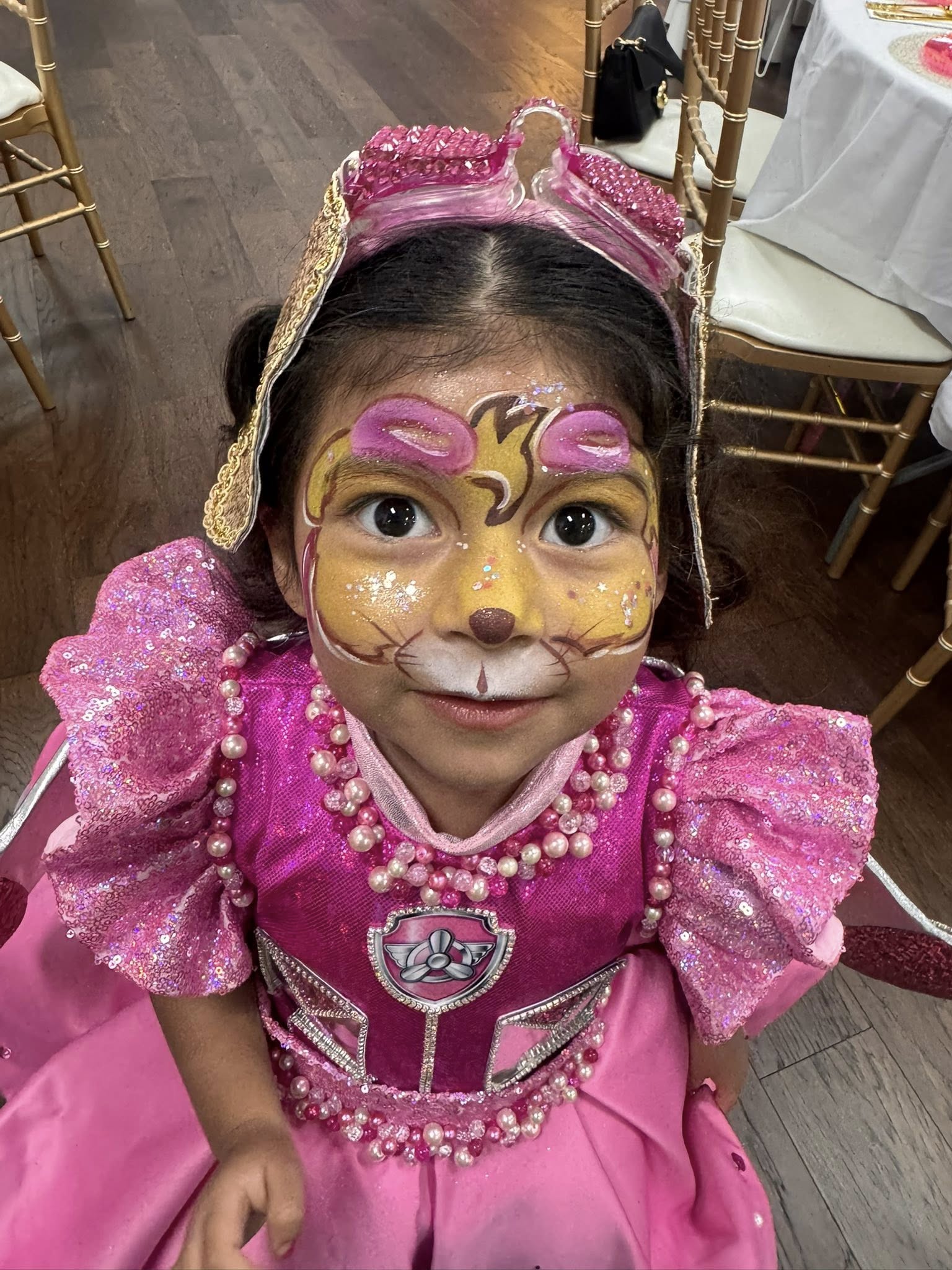 Young girl in a pink sequined Skye Paw Patrol costume with matching face paint and glittery aviator goggles.